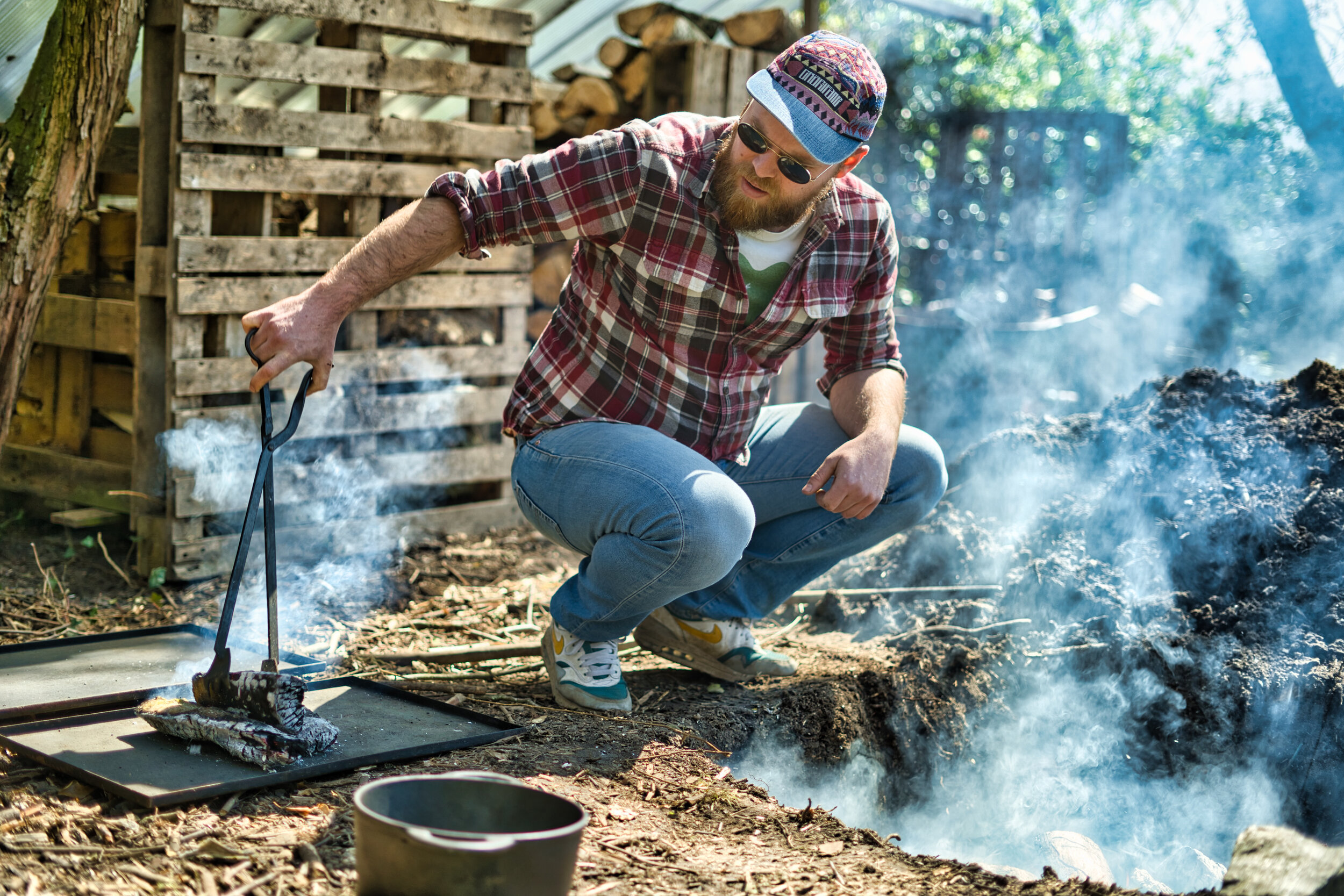Man in houthakkerstijl barbecuet buiten; rook stijgt op.