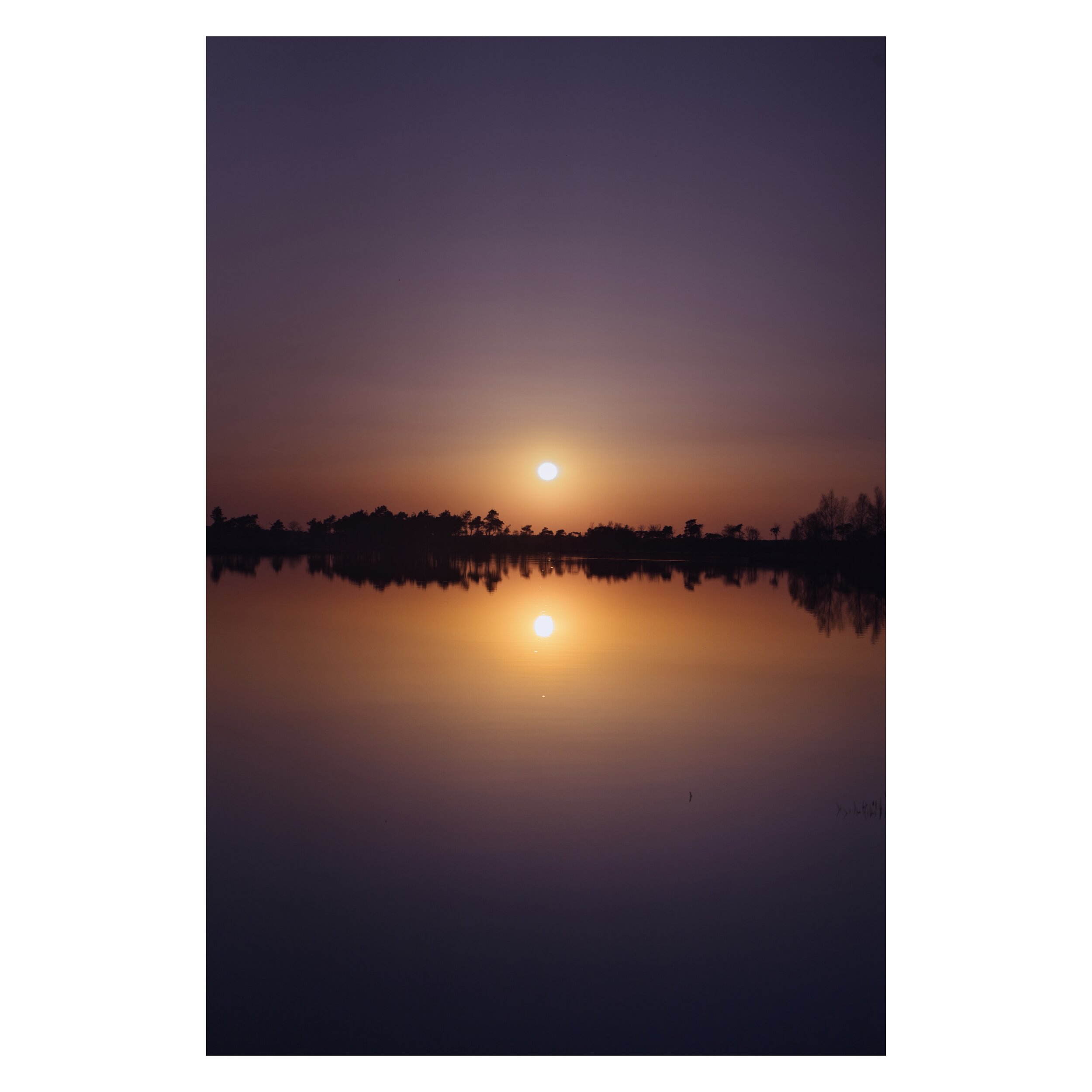 Zonsondergang boven een meer met reflectie, omringd door silhouetten van bomen.