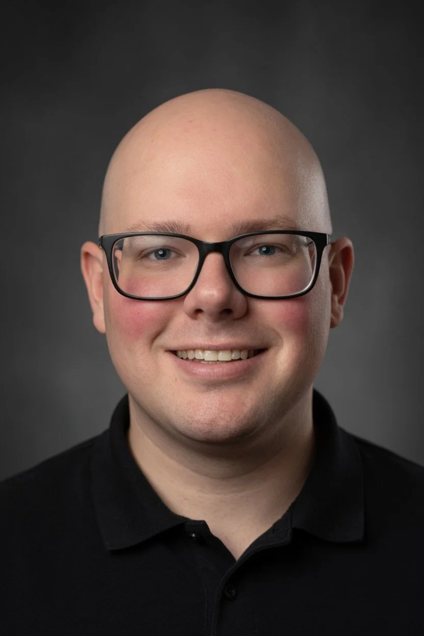 A smiling man wearing glasses and a Reebok shirt at a restaurant with a busy wooden table and other diners in the background.