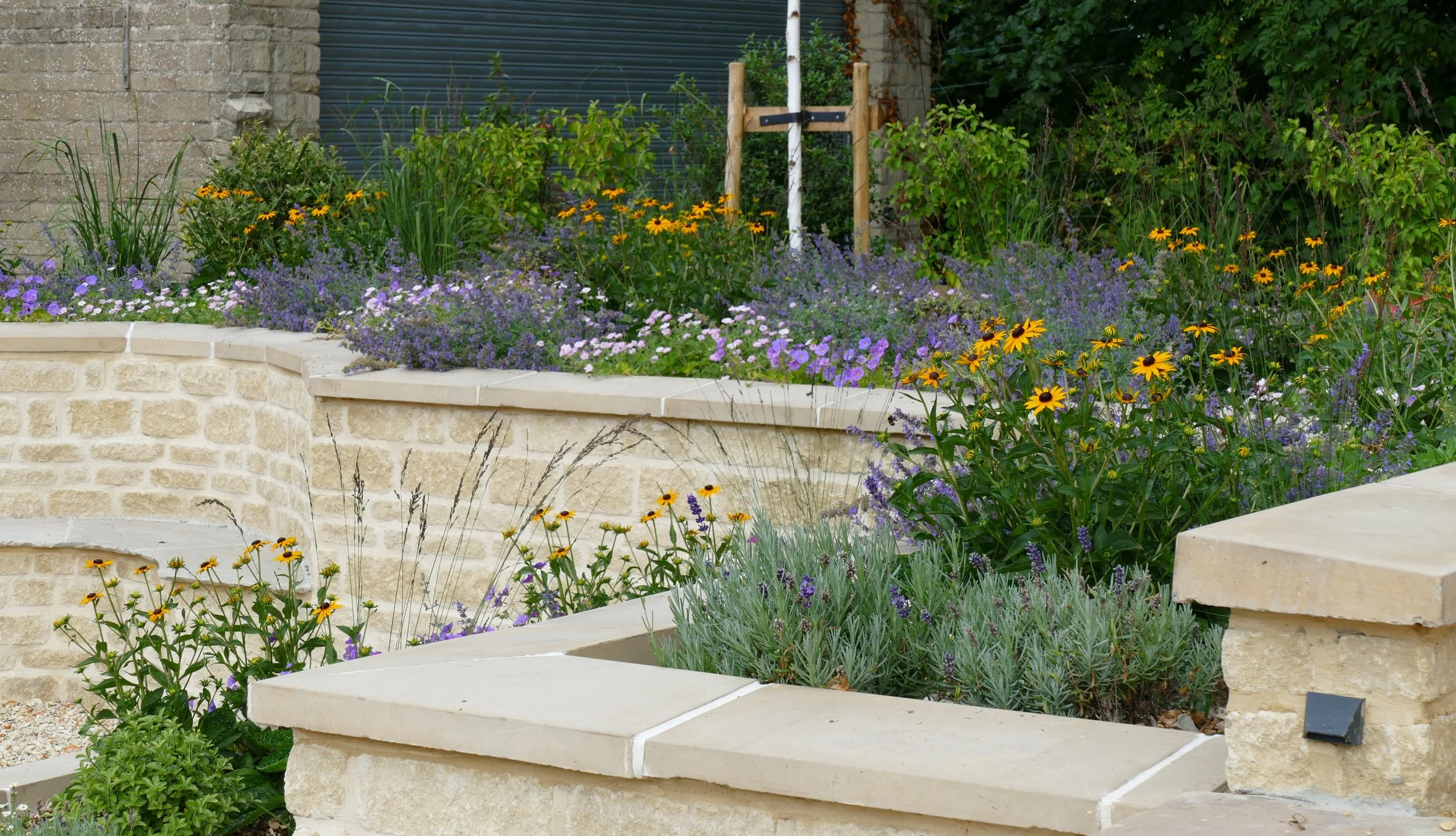 Flower bed with colorful flowers and plants, stone steps and a brick wall in the garden.