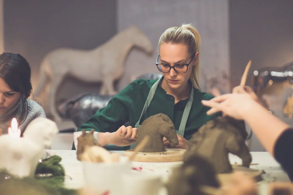 Woman working on a clay sculpture of an horse  at a workshop.