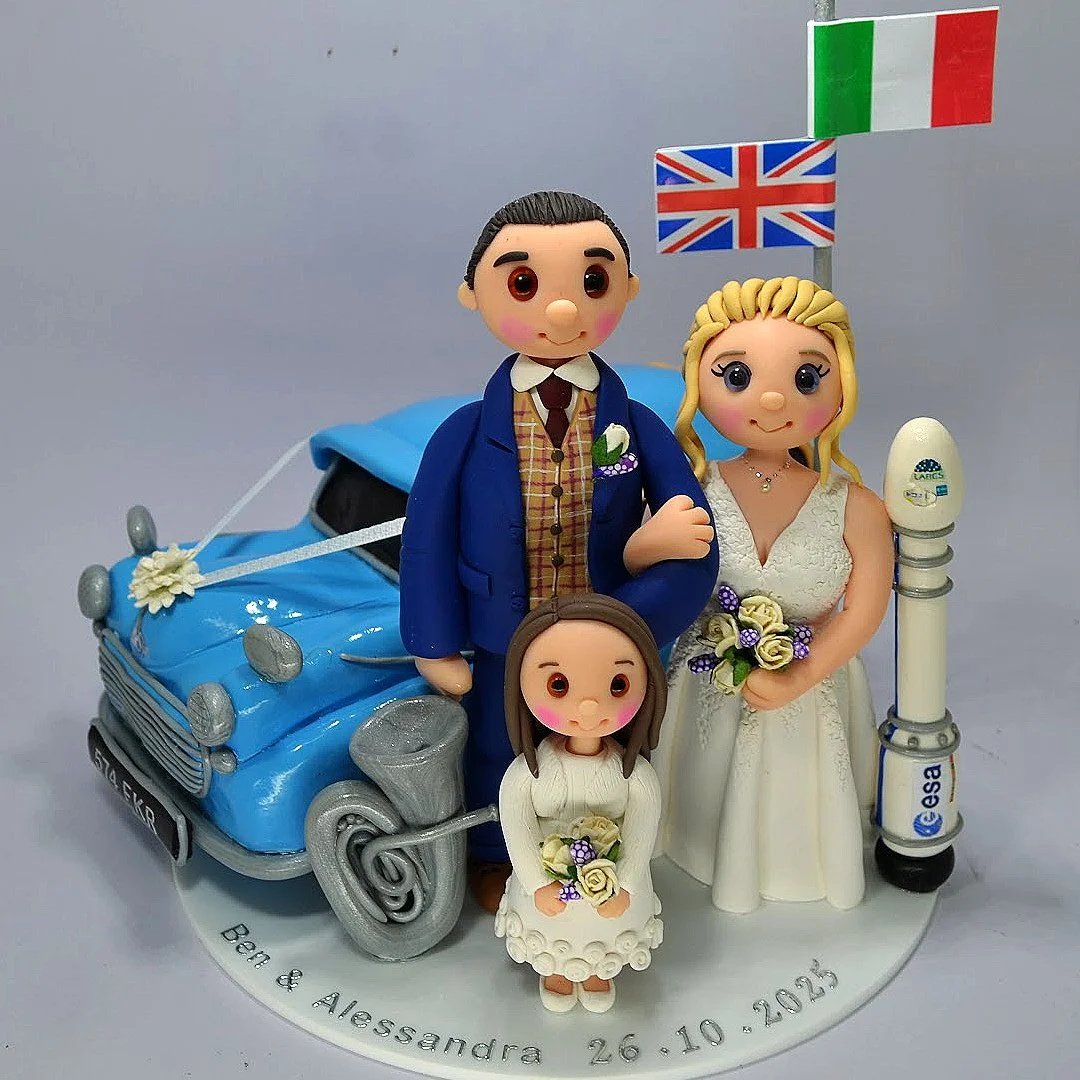 Custom family wedding cake topper featuring bride, groom, child, blue vintage car, tuba instrument and rocket for rocket-scientist bride – handcrafted by TinyLove Wedding Cake Toppers.