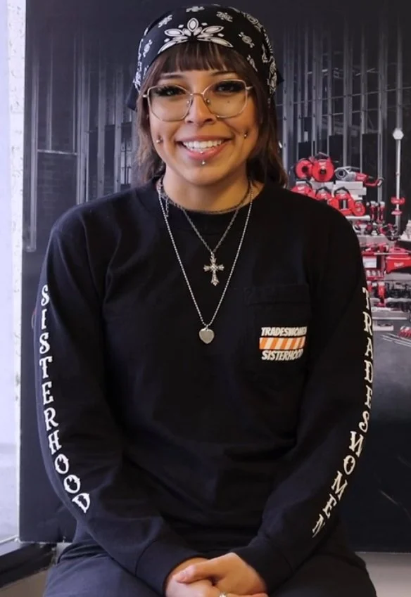 Light skinned woman with piercings on cheeks, lip, and nose in black long sleeved t-shirt and black bandana