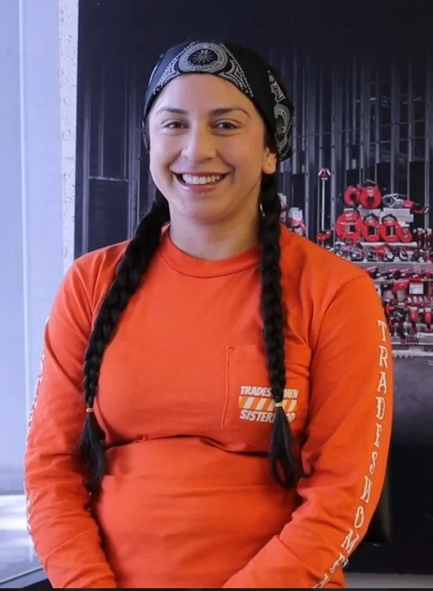 Light skinned woman with long brown braids in an orange long sleeved shirt