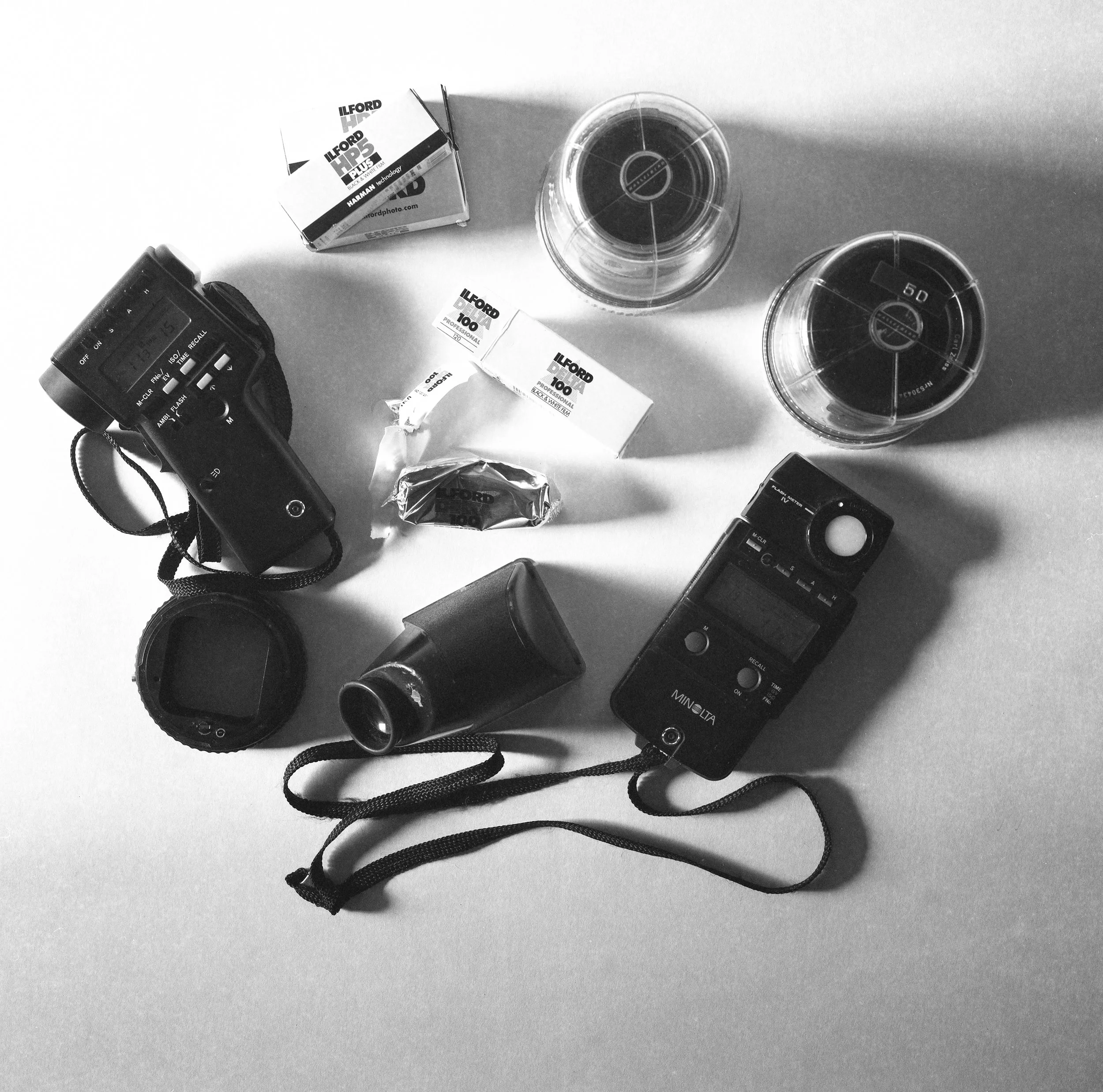 Photography equipment including two cameras, two glasses with drinks, batteries, and small accessories on a plain surface.