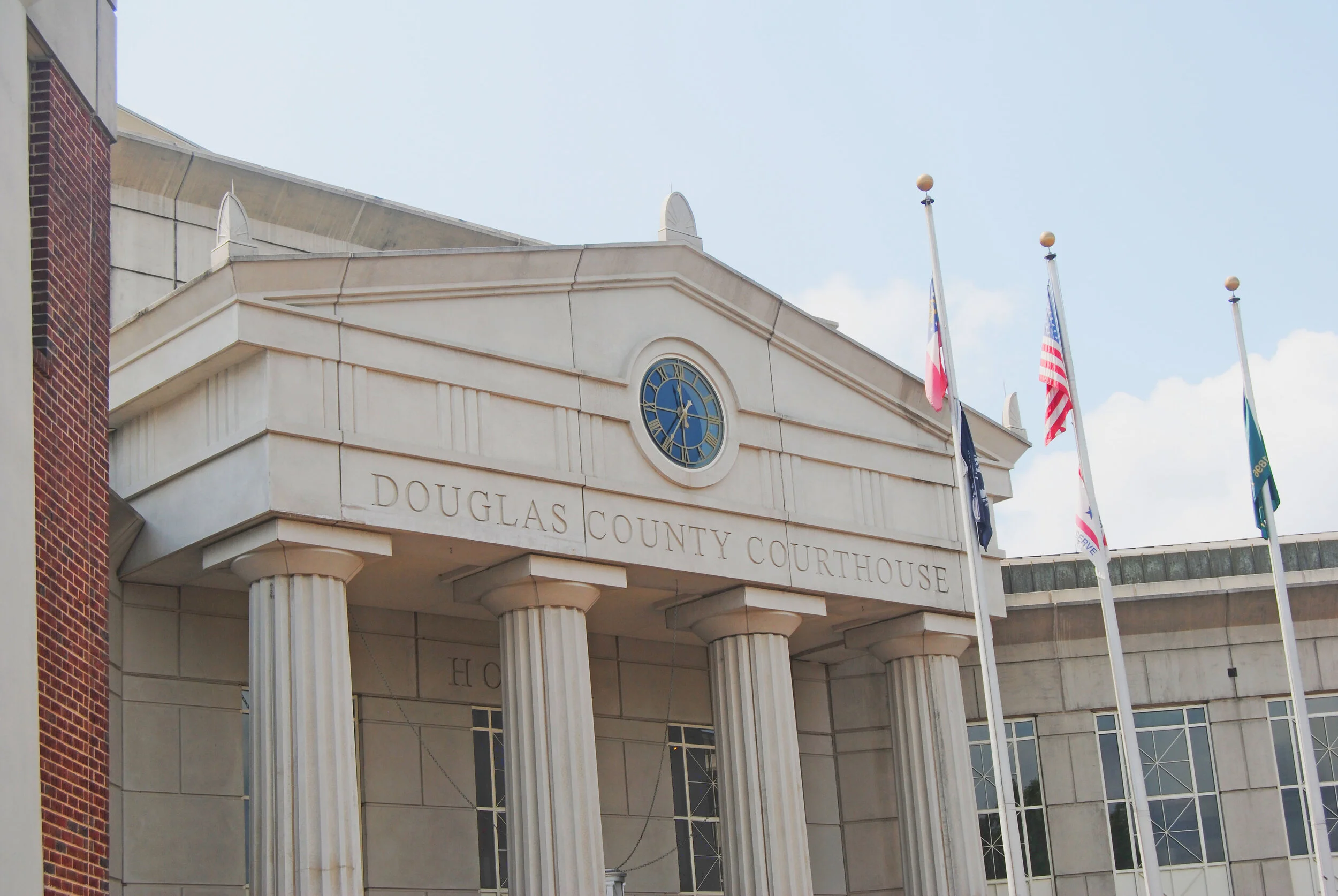 Front entrance of the Douglas County Courthouse. It is a granite building with four large columns with a clock in middle. three flag poles stand outside the building