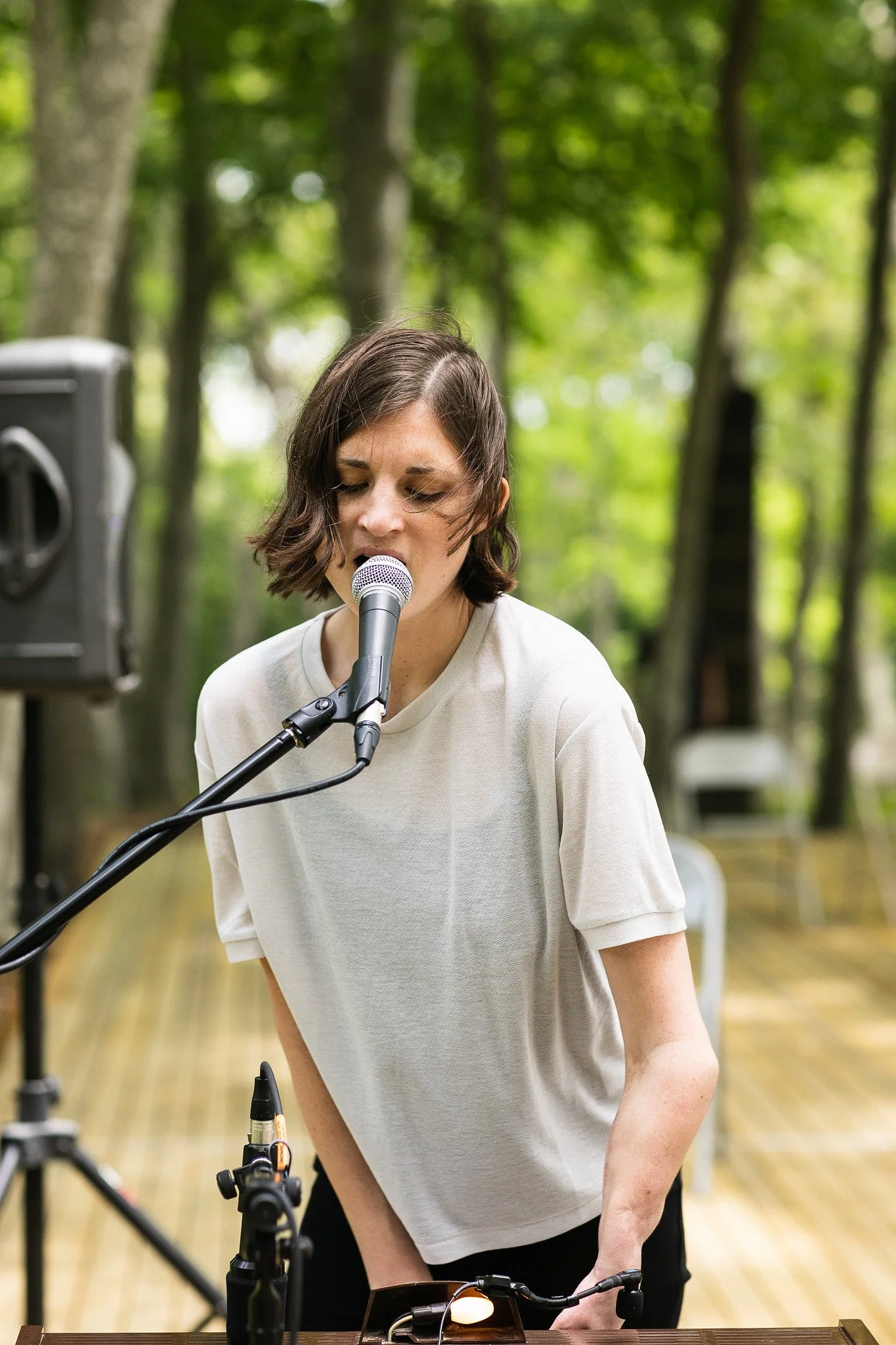 Watermill Community Day, Water Mill, NY. image description: I sign and play at my toy organ, my hair is flowing in the wind and I sing into the vocal mic, with green trees behind me.