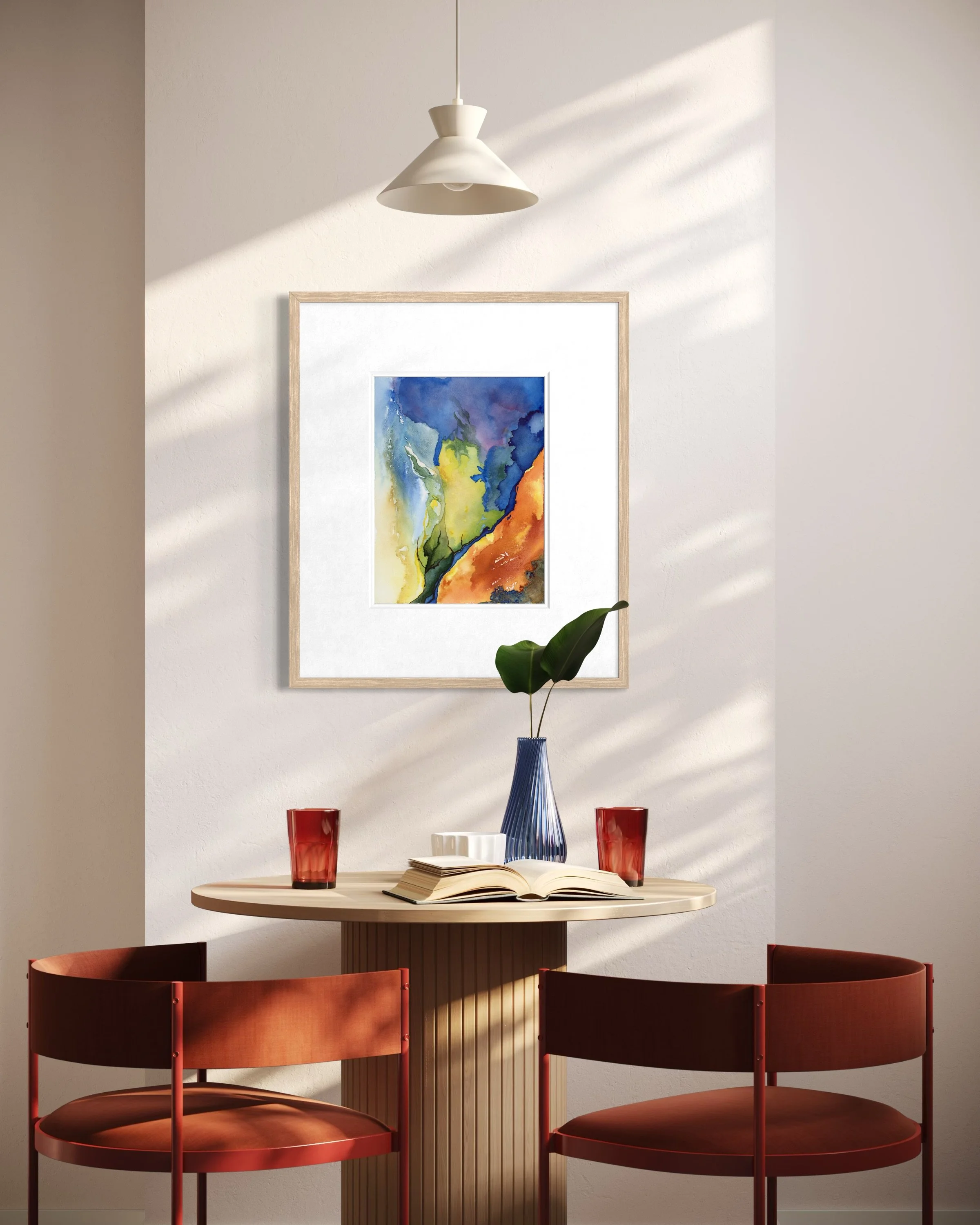 Original watercolor painting with fluid shapes in yellow, orange, blue, and green, framed and hung above a cozy breakfast nook