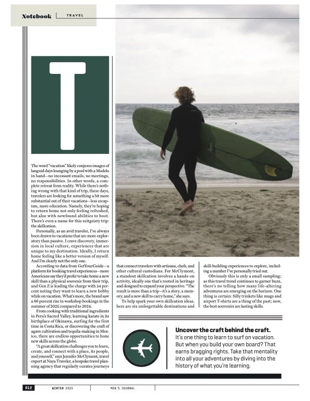 A person in a wetsuit walking on a beach holding a surfboard, with the ocean in the background.