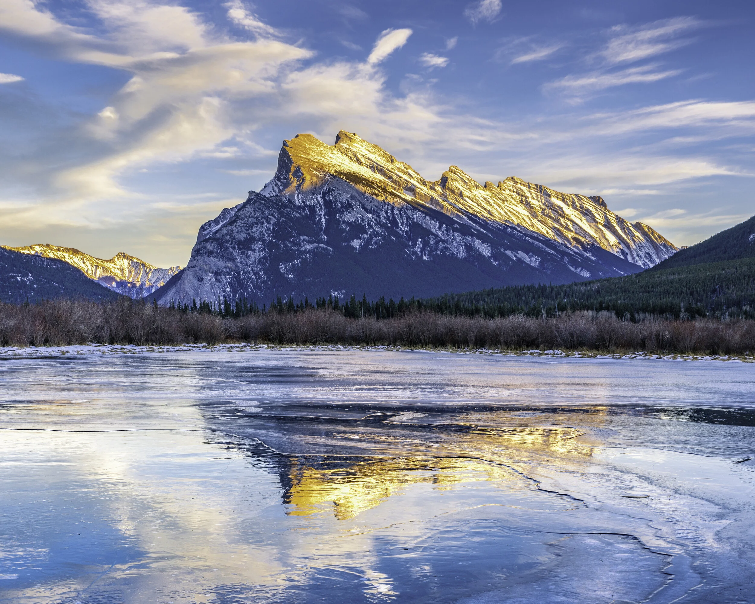 Snow-capped mountain landscape with partly frozen lake in the foreground and a partly cloudy sky