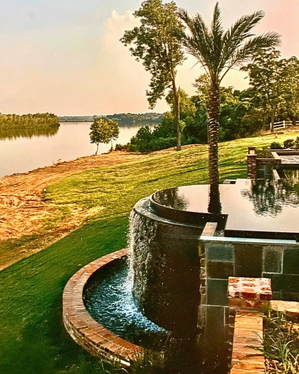 Vanishing edge swimming pool with zero edge spa  designed, engineered and constructed by Waterscapes NWLA.  Spillover catch basin set along the banks of the Red River.  Materials include flagstone deck, rock face spill over and brick catch basin.