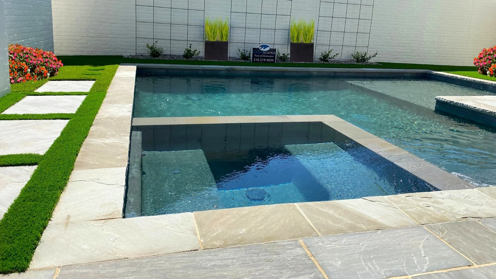 Intimate swimming pool and spa designed and built by Waterscapes of Shreveport.  This pool and spa features artificial turf with flagstone decking and pool coping.  Aerators were installed to assist with pool cooling.  There is also a seating and tan