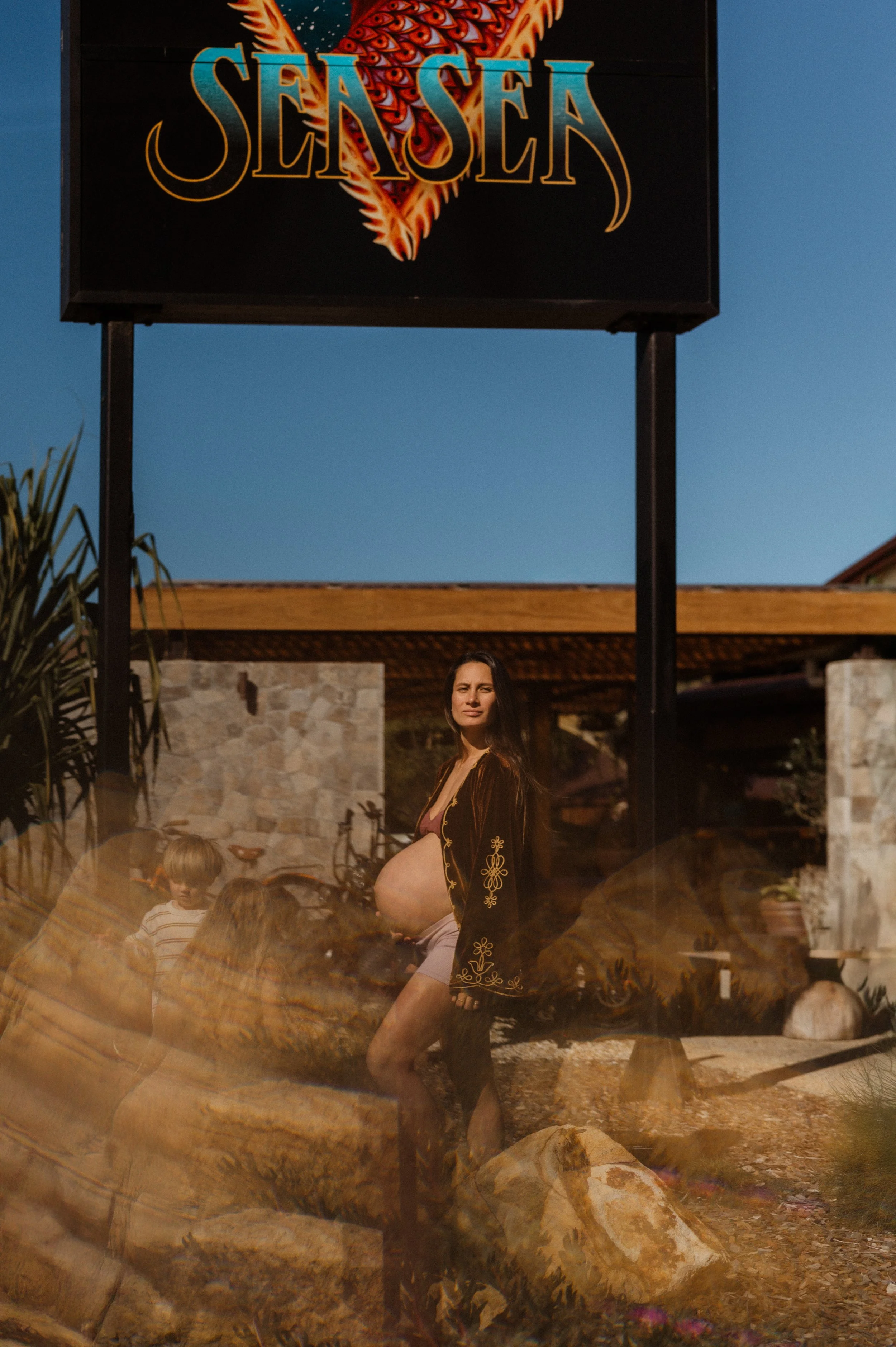 A photo of a pregnant woman standing outdoors in front of a retro hotel.