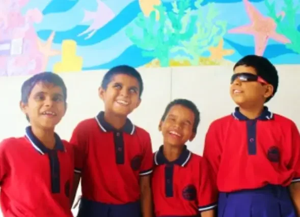 Four children in red school uniforms smiling, standing in front of an underwater-themed mural with coral, fish, and starfish.