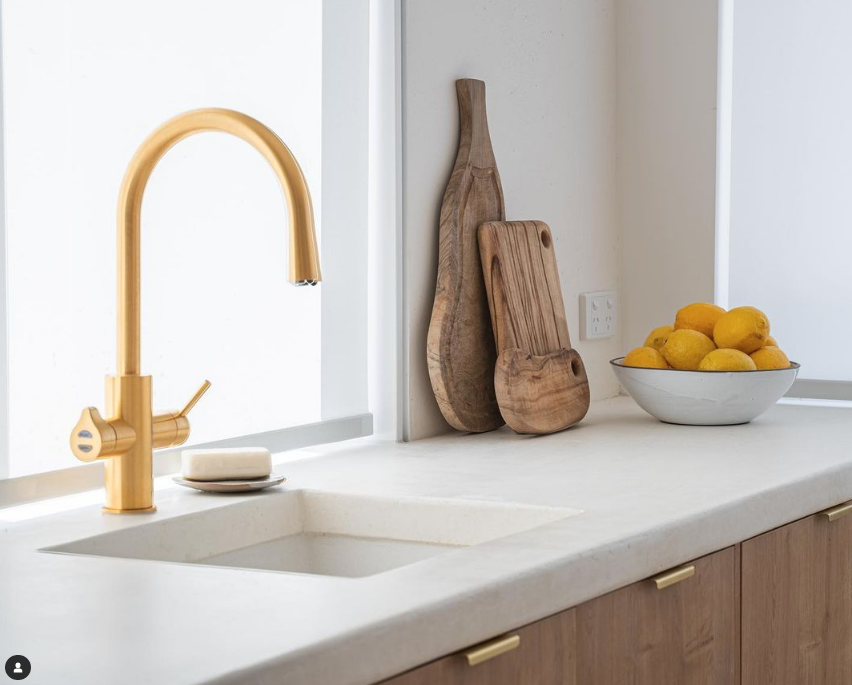 Modern kitchen counter with a gold faucet, wooden cutting boards, and a bowl of lemons.