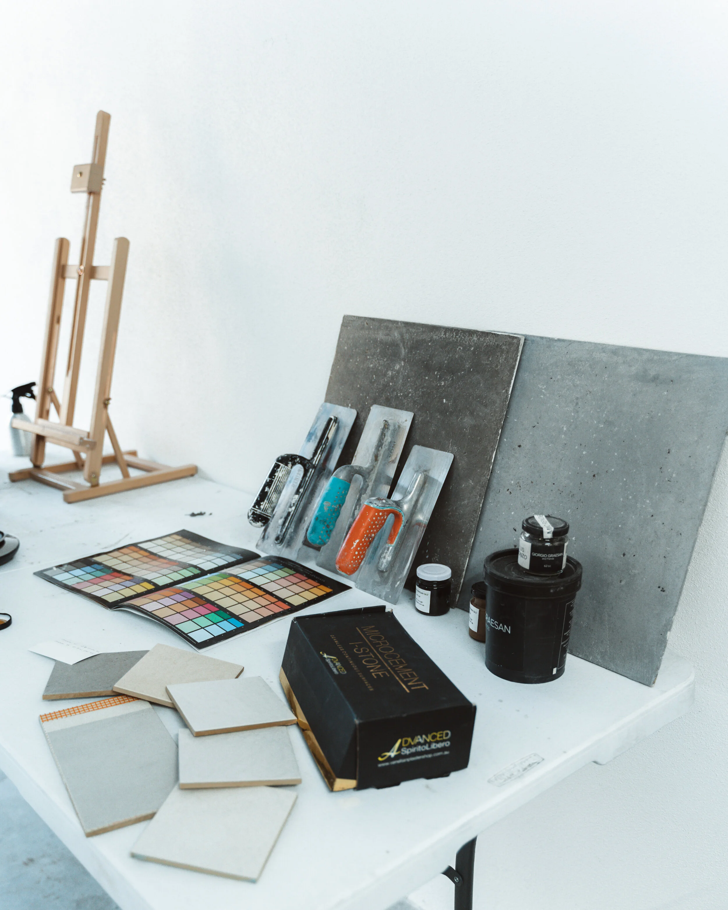 Art supplies on a table with paint swatches, trowels, tiles, and an easel.