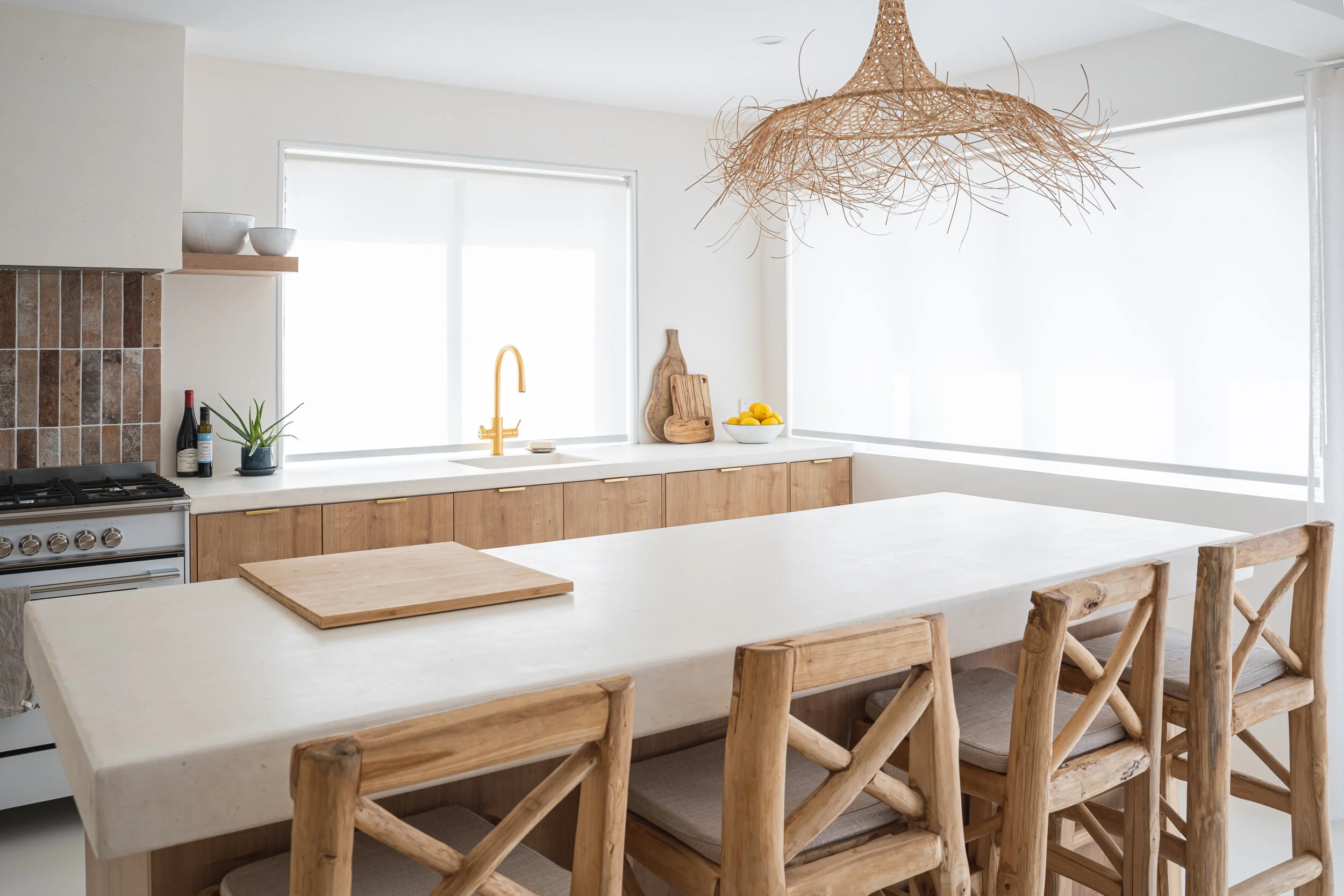 Modern kitchen with wooden furniture, white countertops, a gold faucet, a large pendant light, and a decorative bowl of lemons.