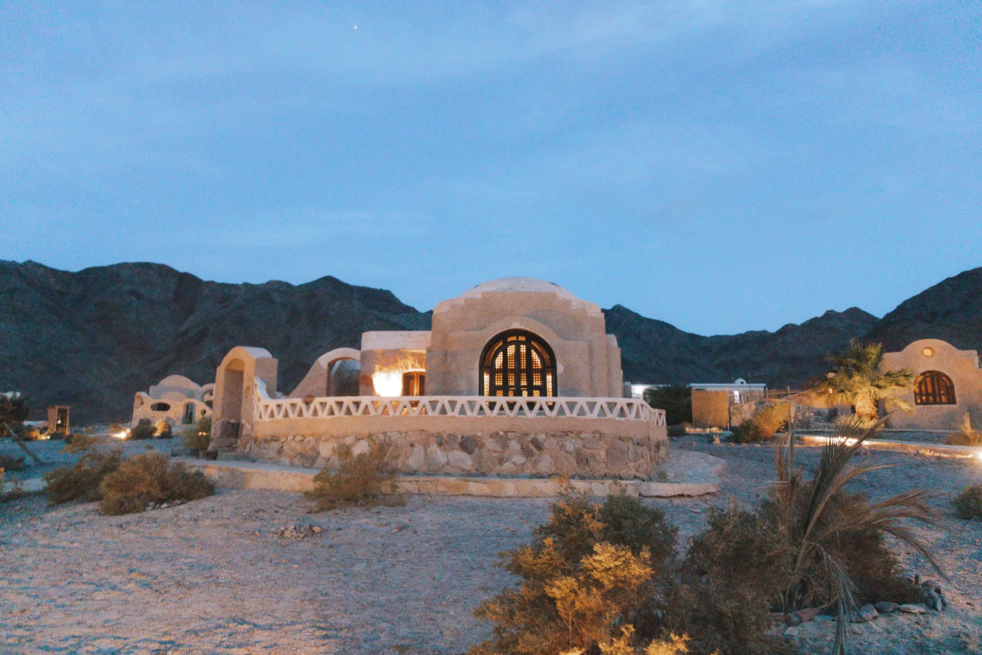 Desert village with dome-shaped stone buildings and a mountainous background at dusk.
