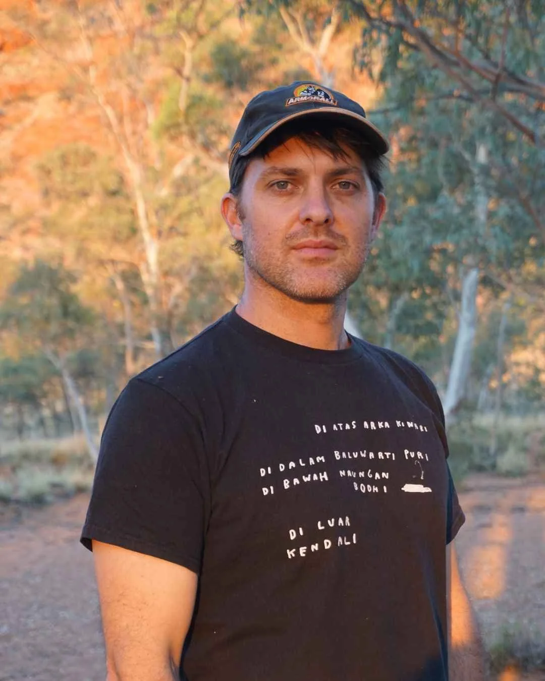 Portrait of Australian artist Jack Hodges outdoors in a bushland setting, wearing a black T-shirt and cap. Selected artist for the LANTANA Space Artist Residency Program 2026/27.