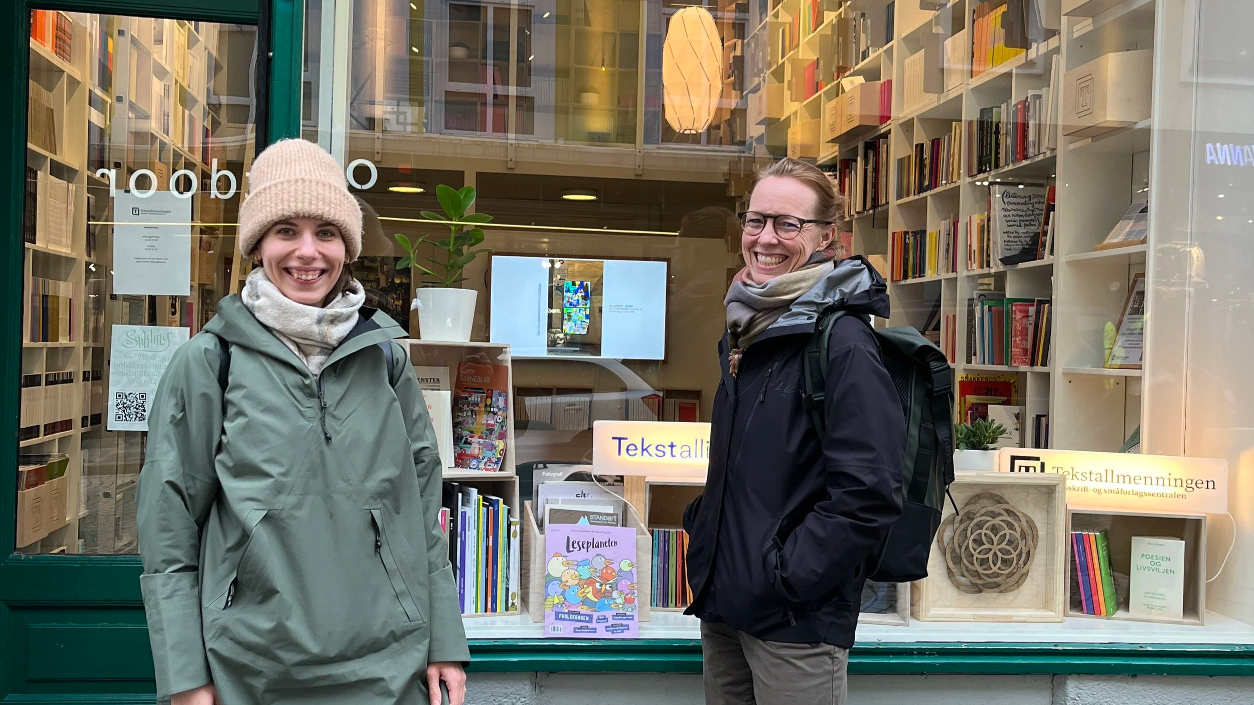 Two smiling women standing outside in front of a bookstore window.