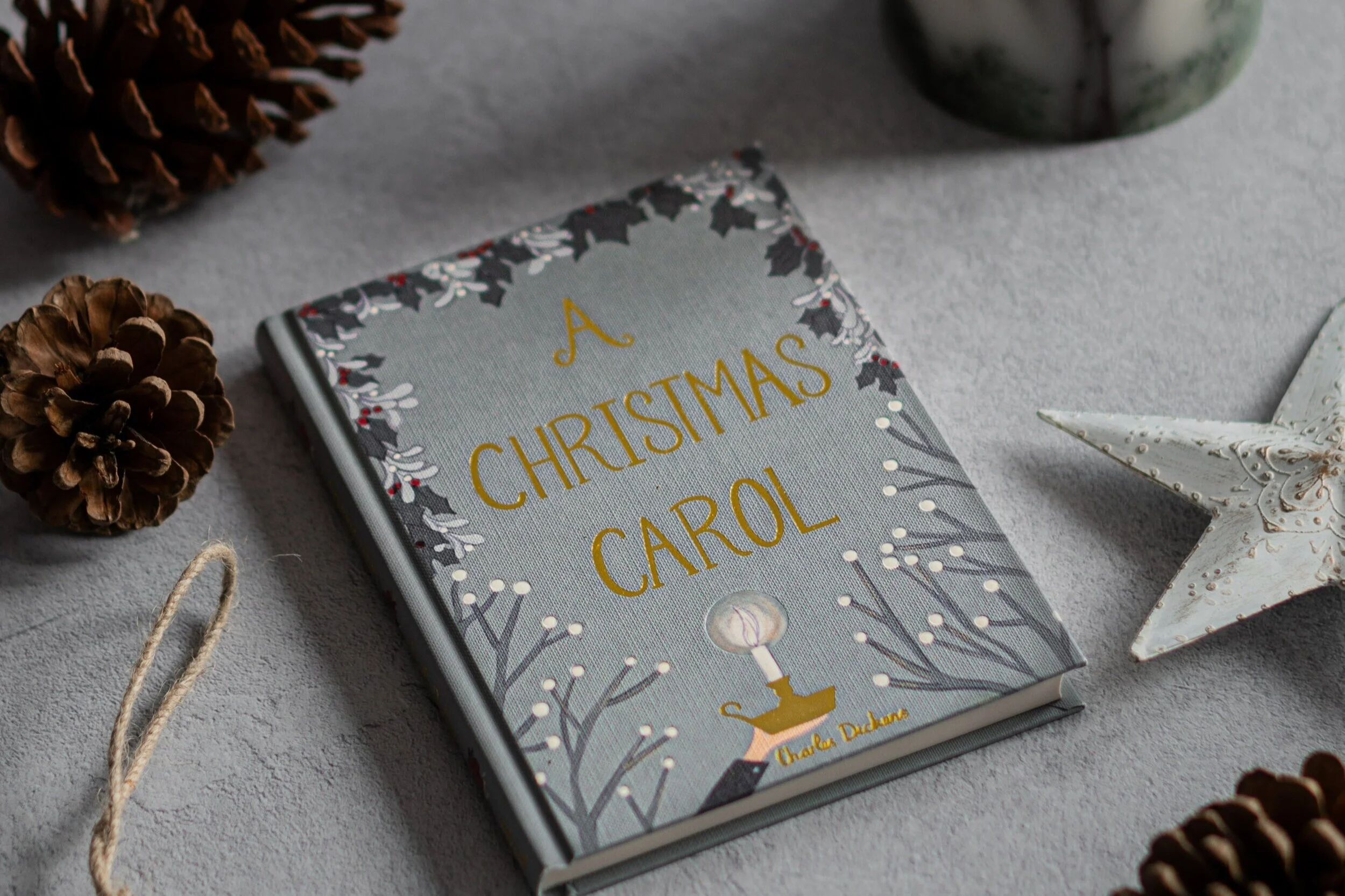 A book with an engraved title of, "A Christmas Carol". Pinecones and a star ornament surround the book.
