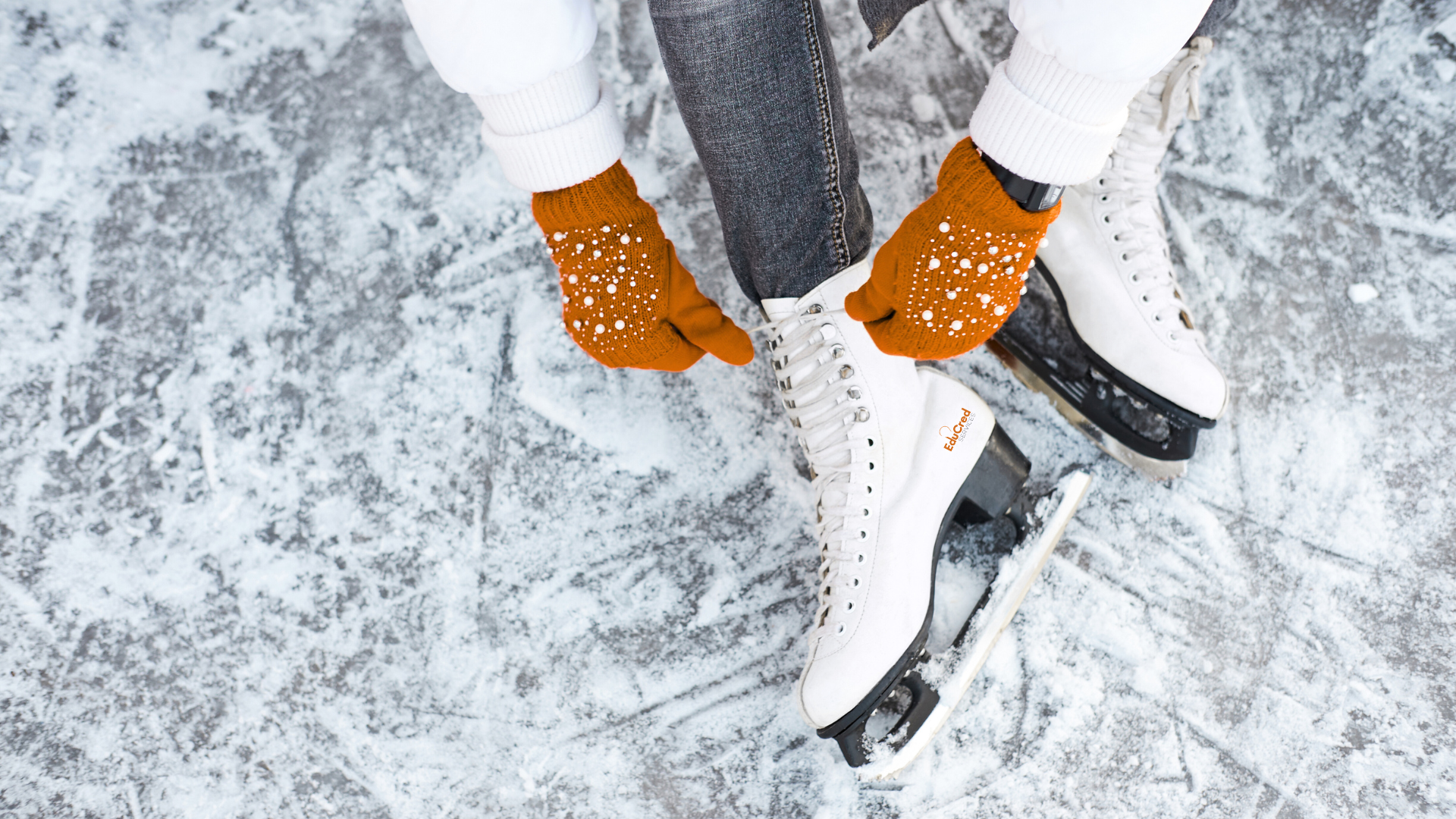 A woman in orange gloves laces up a pair of figure skates.