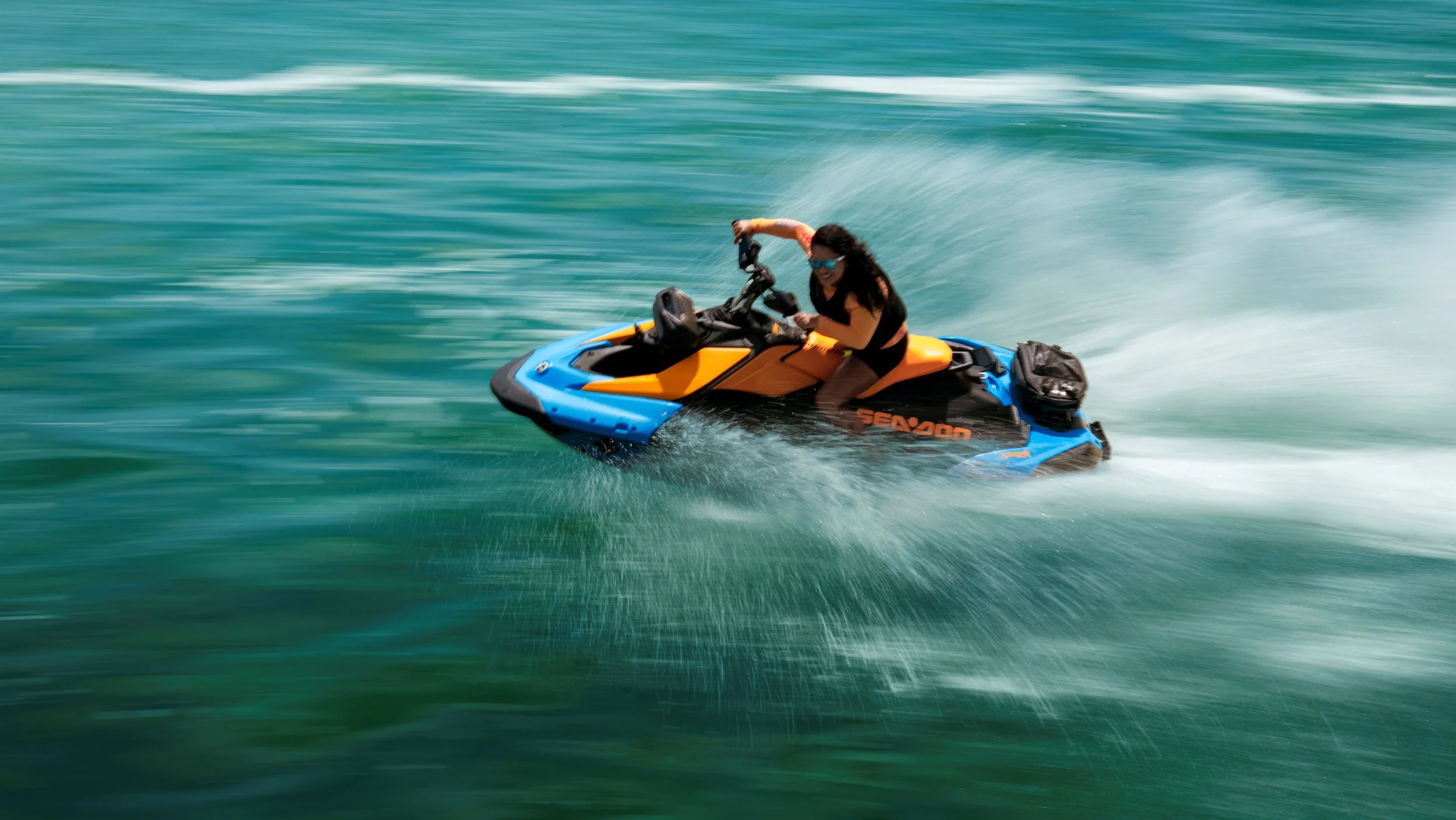 Woman riding a blue and orange Seadoo Spark Trixx jet ski on the water