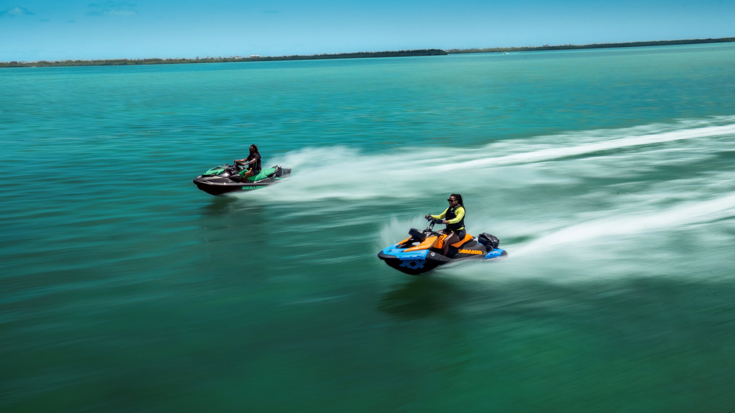 Two people riding Sea-Doo jet skis on clear blue water in a tropical setting. Seadoo Trixx and Sea-Doo GTI
