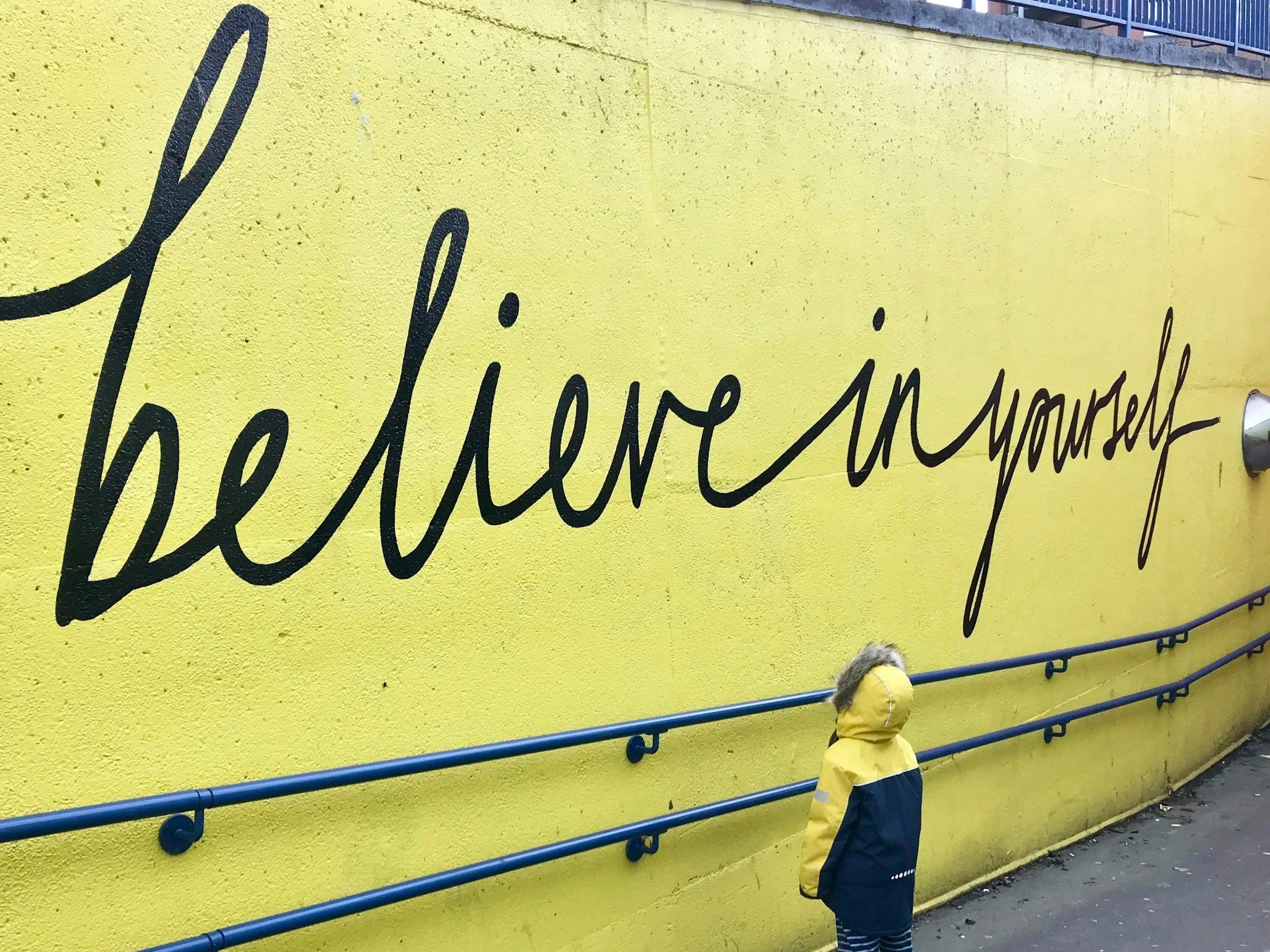 A child looking up at a yellow sign that says "believe in yourself"