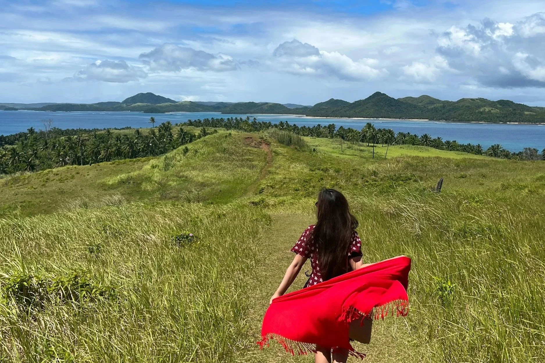 Woman in a dress walking through a field with a beautiful landscape with hills and the ocean