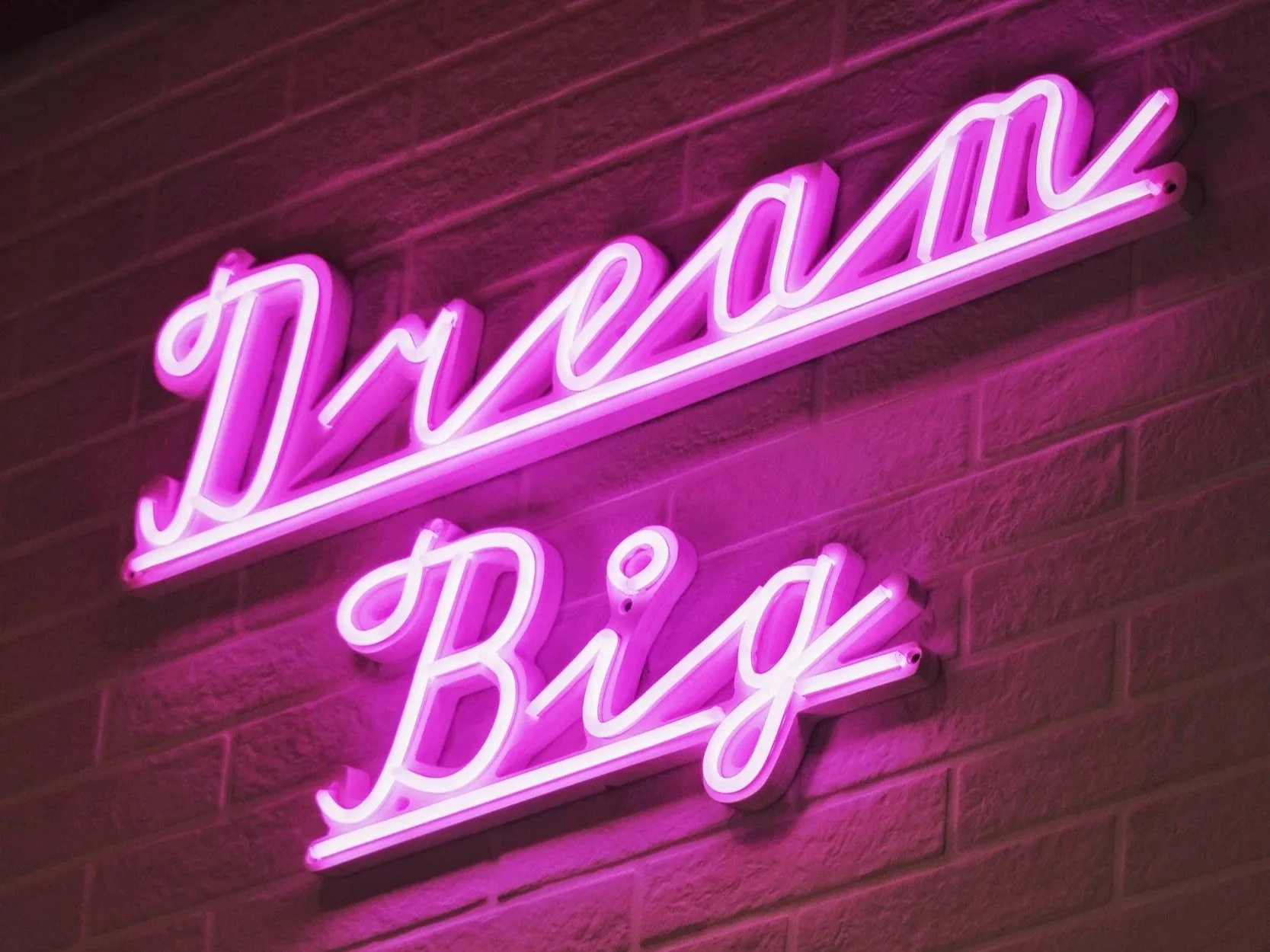 Pink neon sign on a wall that says "Dream Big"