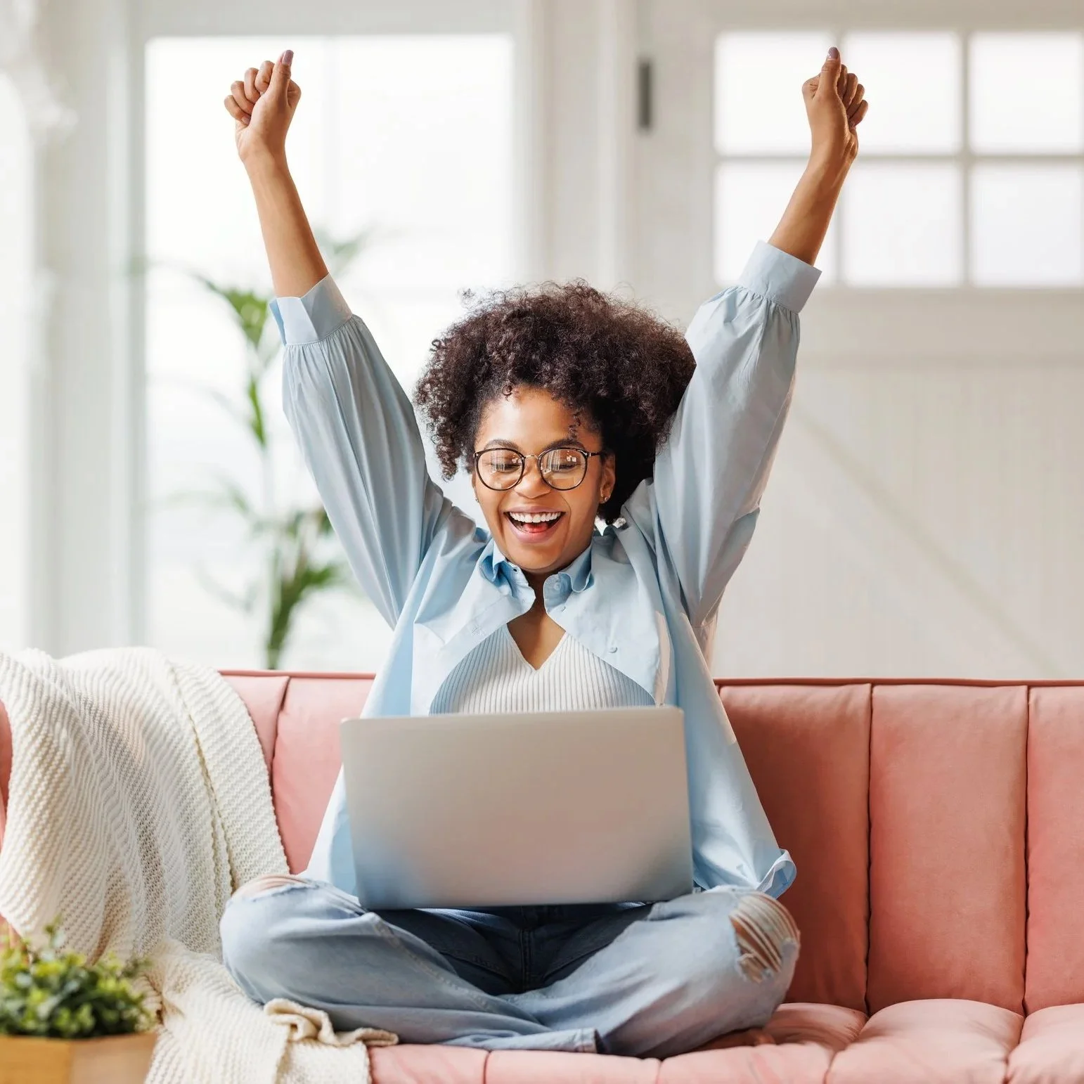 Excited woman with her hands up in the air as she sits on her couch with her laptop