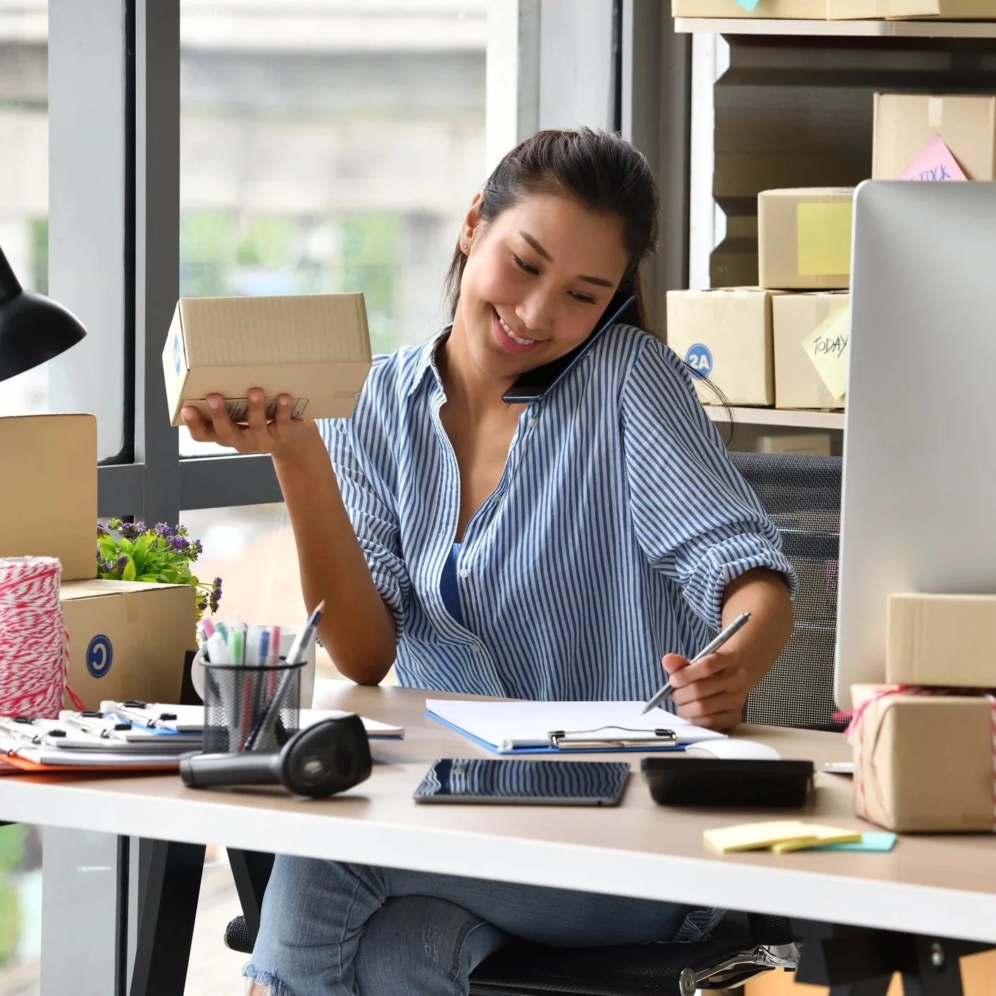 Woman busy in her business packing up boxes to send and she's on the phone smiling
