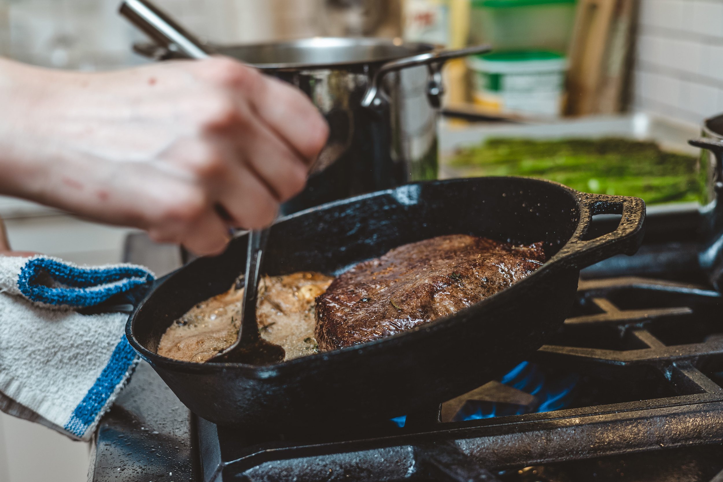 Private chef basting steak in a cast iron pan in a private residence.