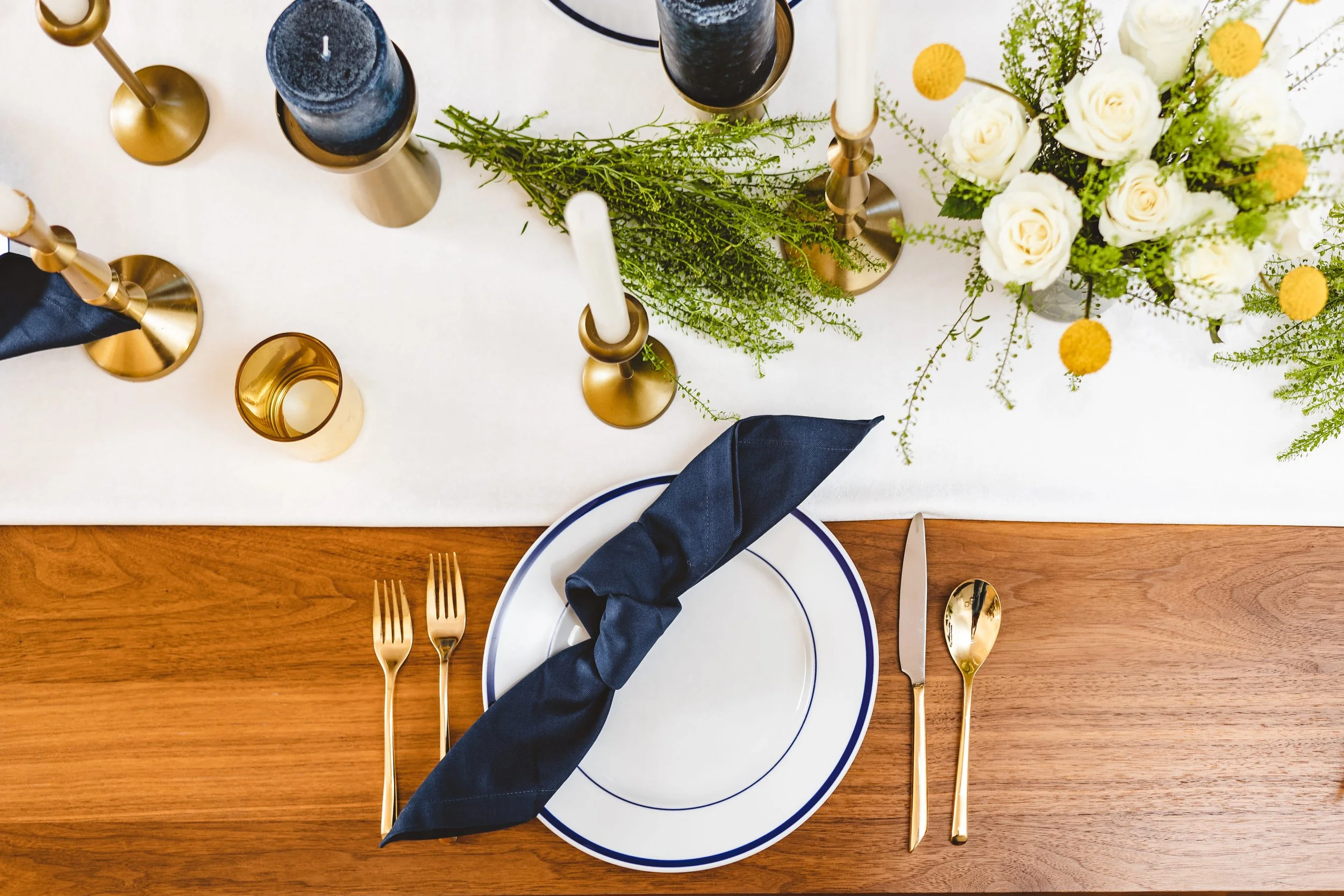 Elegant dinner party place setting with navy napkin and gold cutlery in a private home.