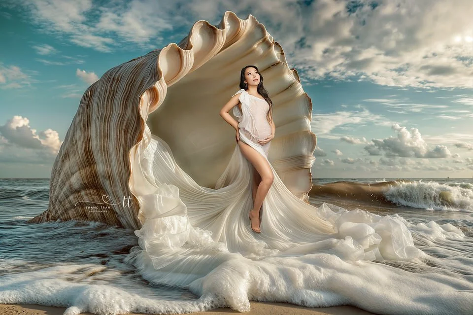 Denver maternity photography – fine art portrait of an expectant mom in a flowing white gown, standing in a giant seashell by the ocean.