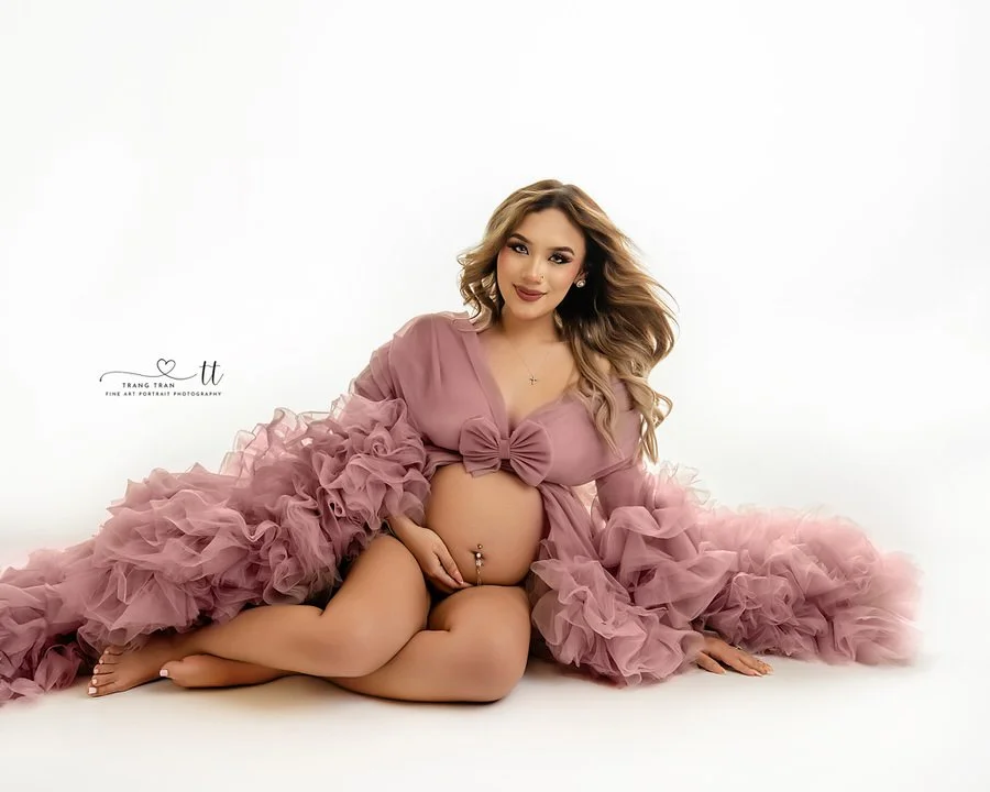 Broomfield studio maternity session, seated mom in dusty rose ruffled robe on a clean white set, relaxed smile and hands on belly.