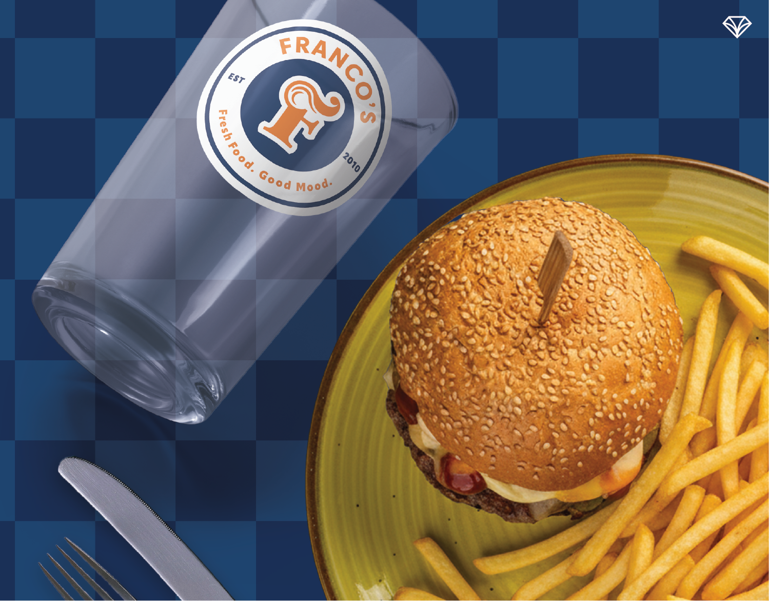 A cheeseburger and fries on a plate next to a branded Franco's glass.