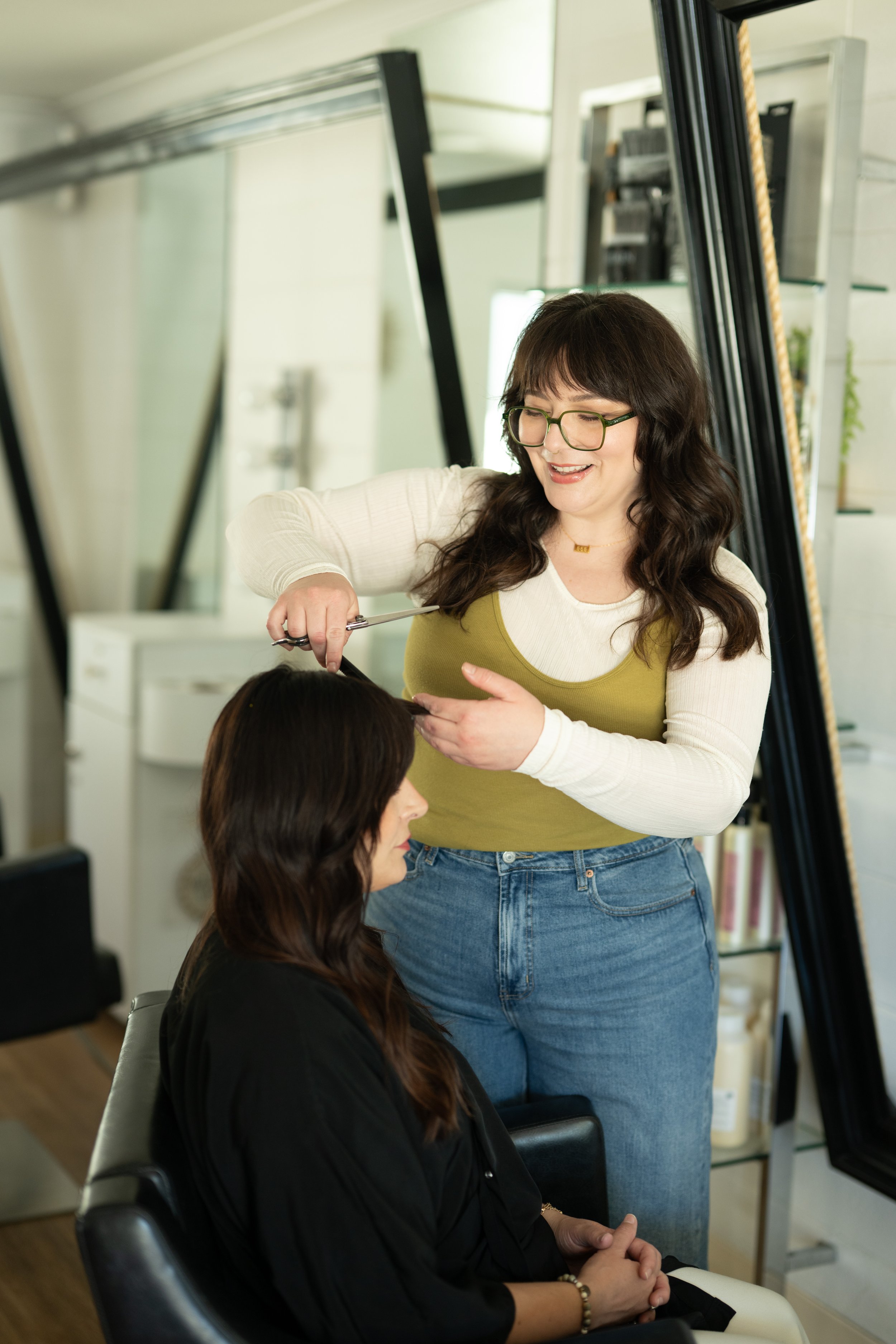 A person getting their hair cut, with a hairstylist holding scissors and cutting long, dark, wet hair. A clip is used to section the hair on top of the head.