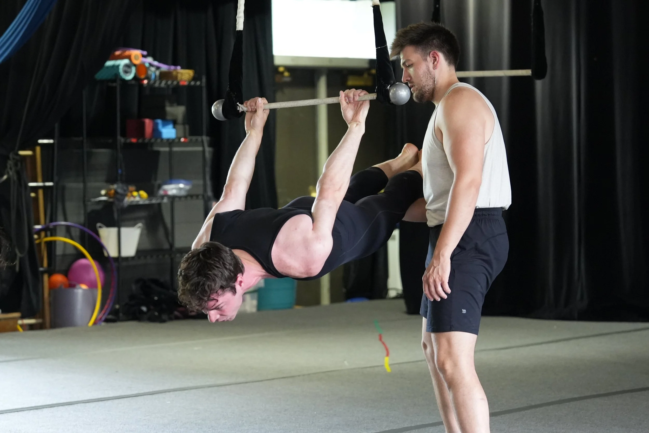 An instructor assists a woman hanging from a lyra
