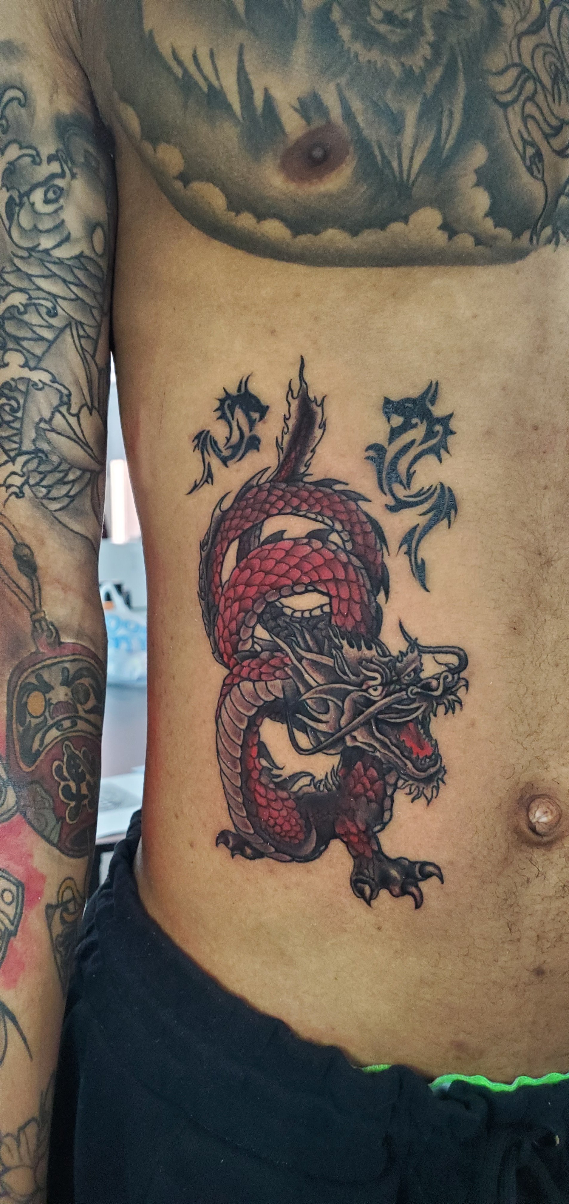 Tattoo of a red and black dragon on person's side, breathing fire.