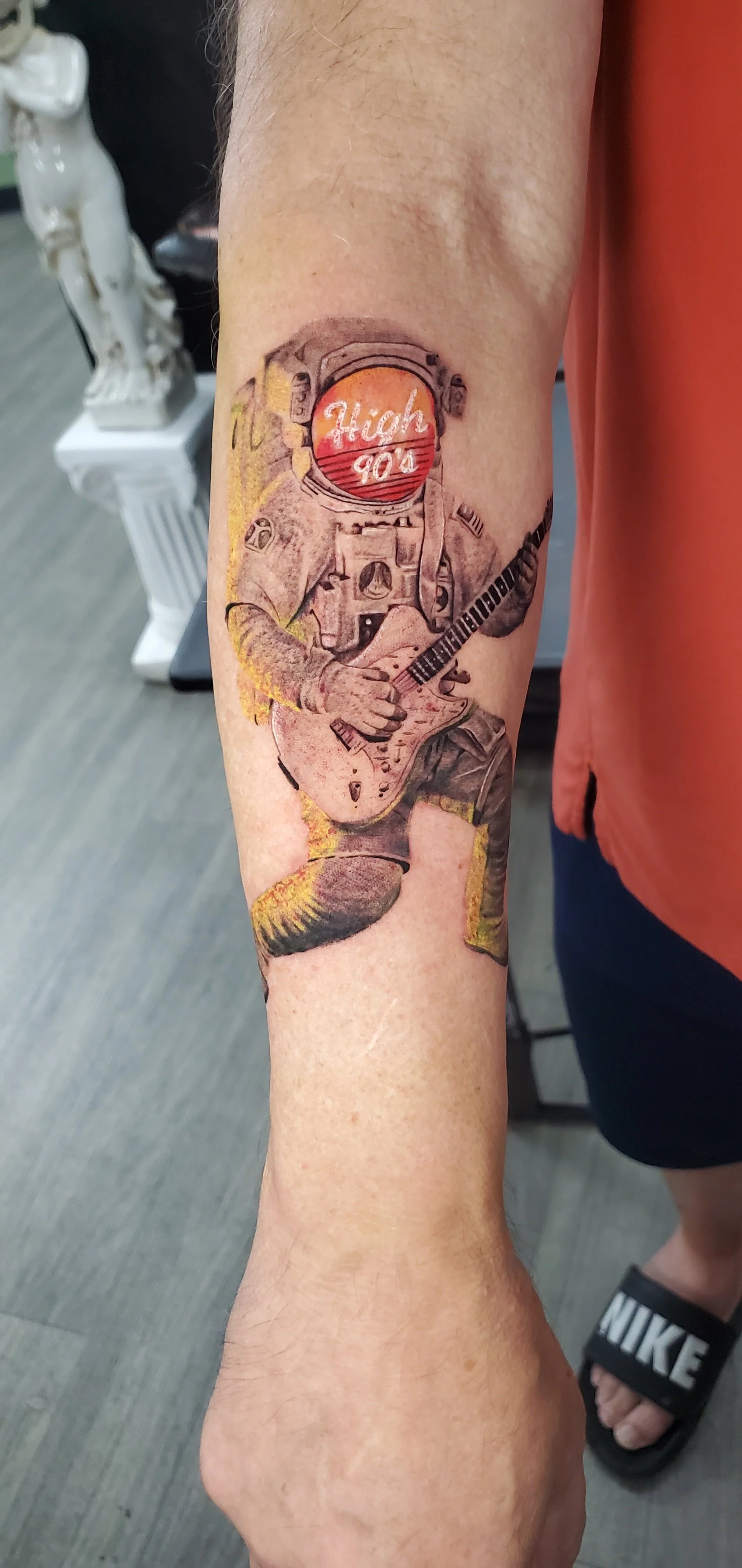 Tattoo of an astronaut playing an electric guitar, with a sunset in the helmet reflecting the words 'High' and '900'.