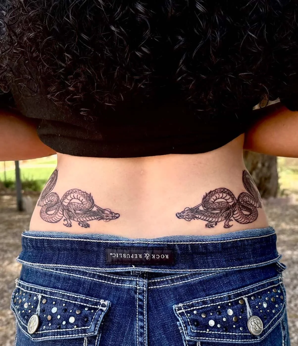 Tattoo of two grass snakes on the lower back of a person wearing blue jeans.