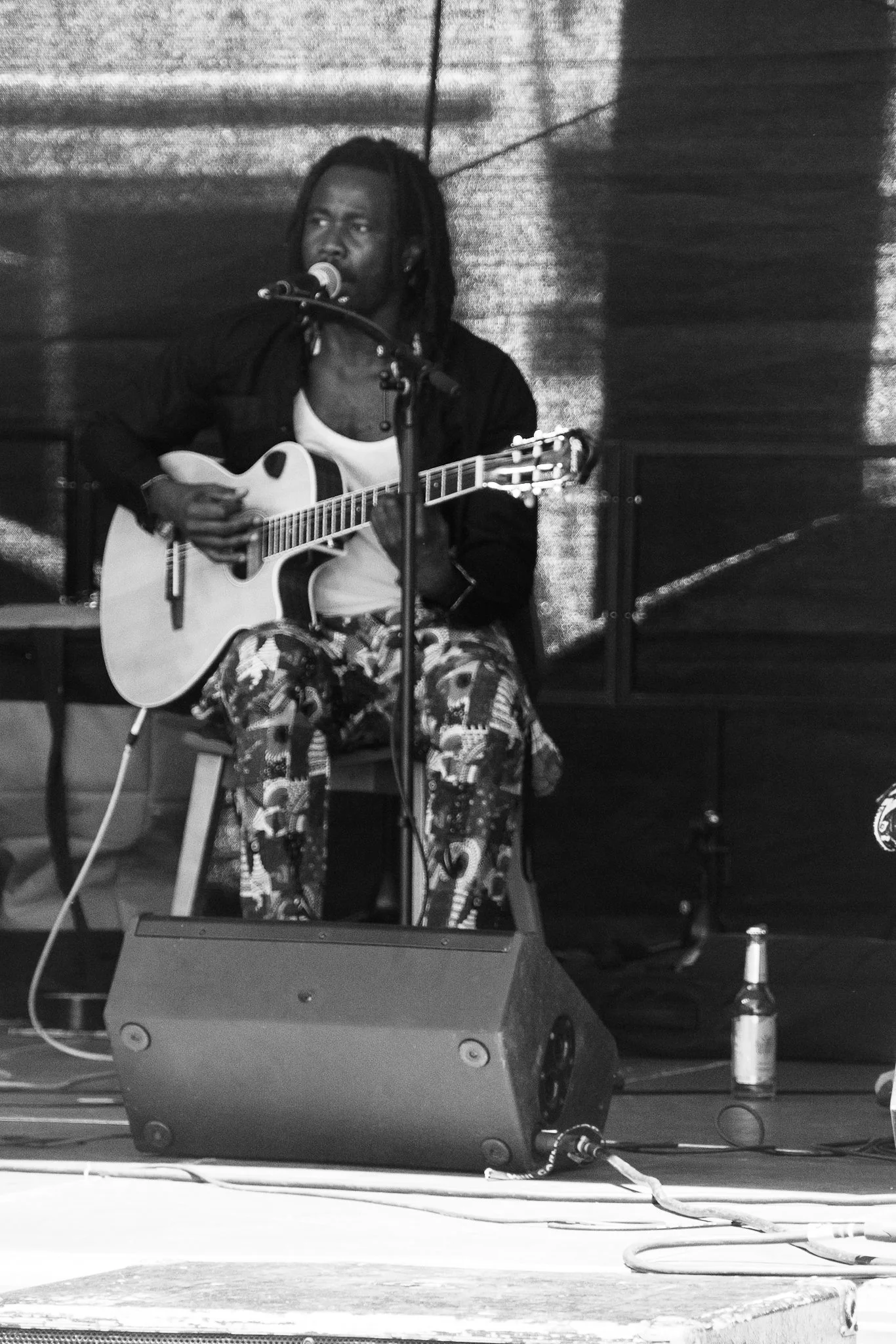 Ein Musiker spielt Gitarre und singt an einem Mikrofon auf einer Bühne, schwarz-weiß Aufnahme.