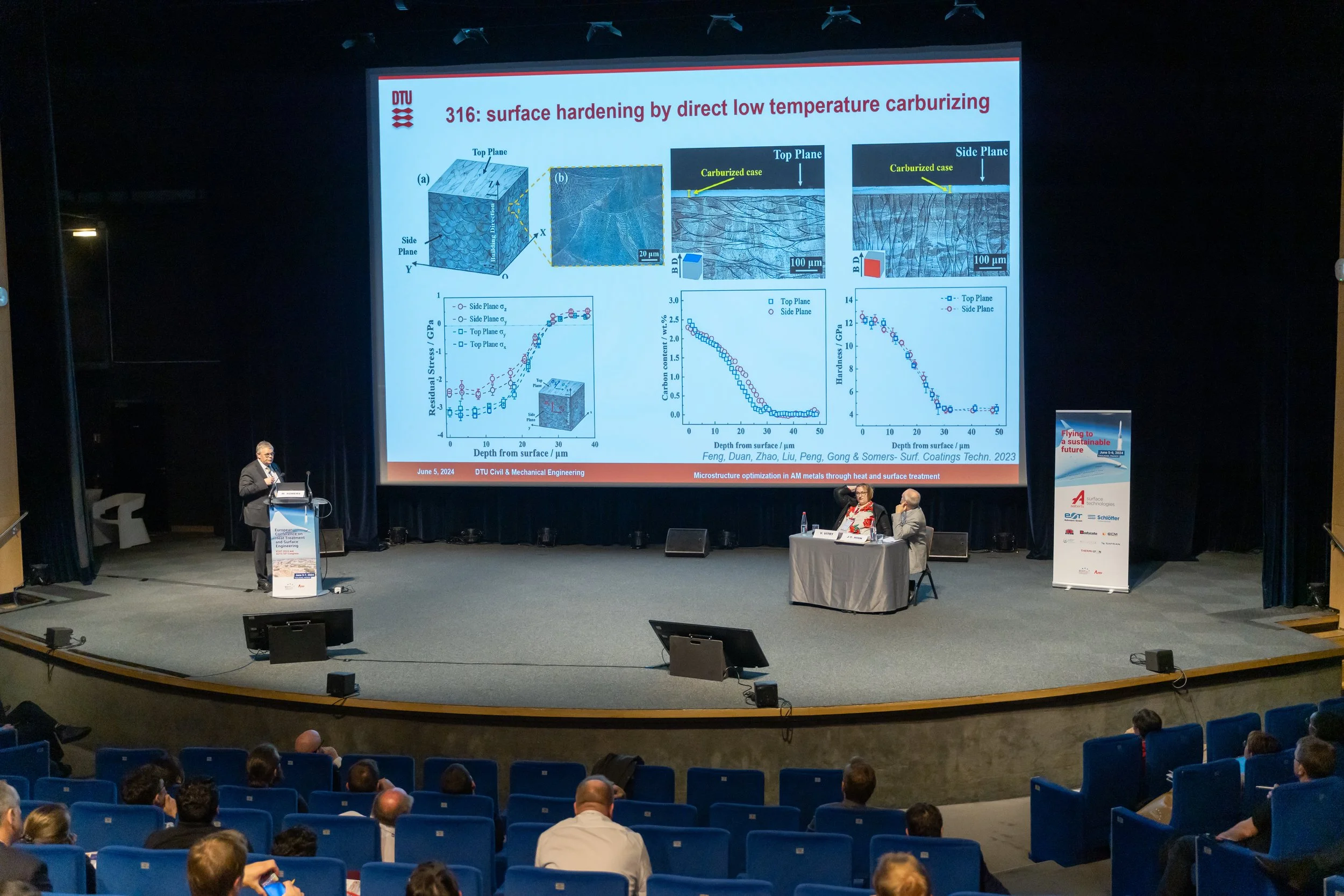 Conférence avec présentation sur le durcissement de surface par carbonitruration à basse température. Diapositives projetées, orateurs et public dans un auditorium.