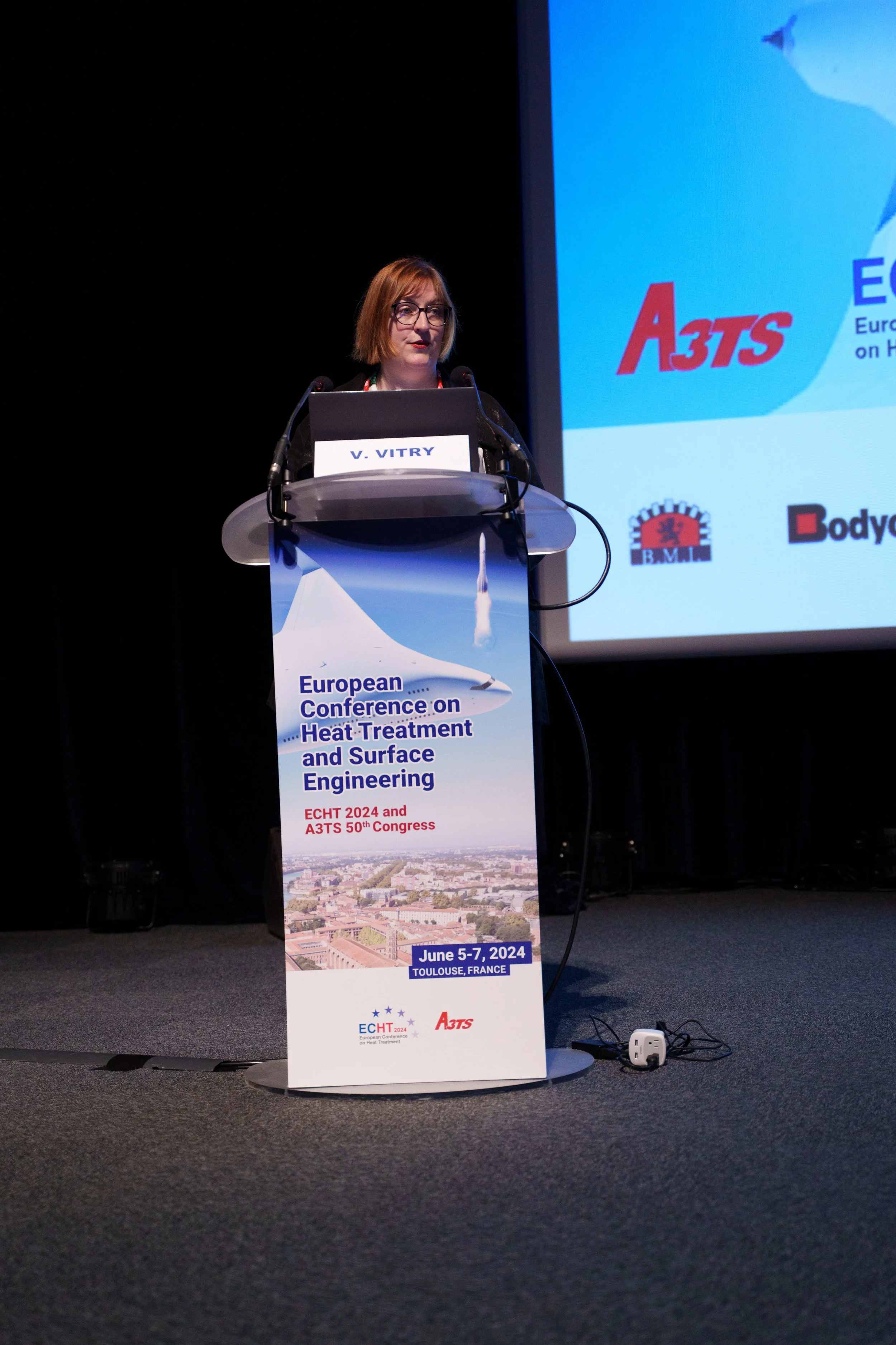 Conférencier à la tribune lors de la conférence européenne sur le traitement thermique et l'ingénierie de surface 2024 à Toulouse.