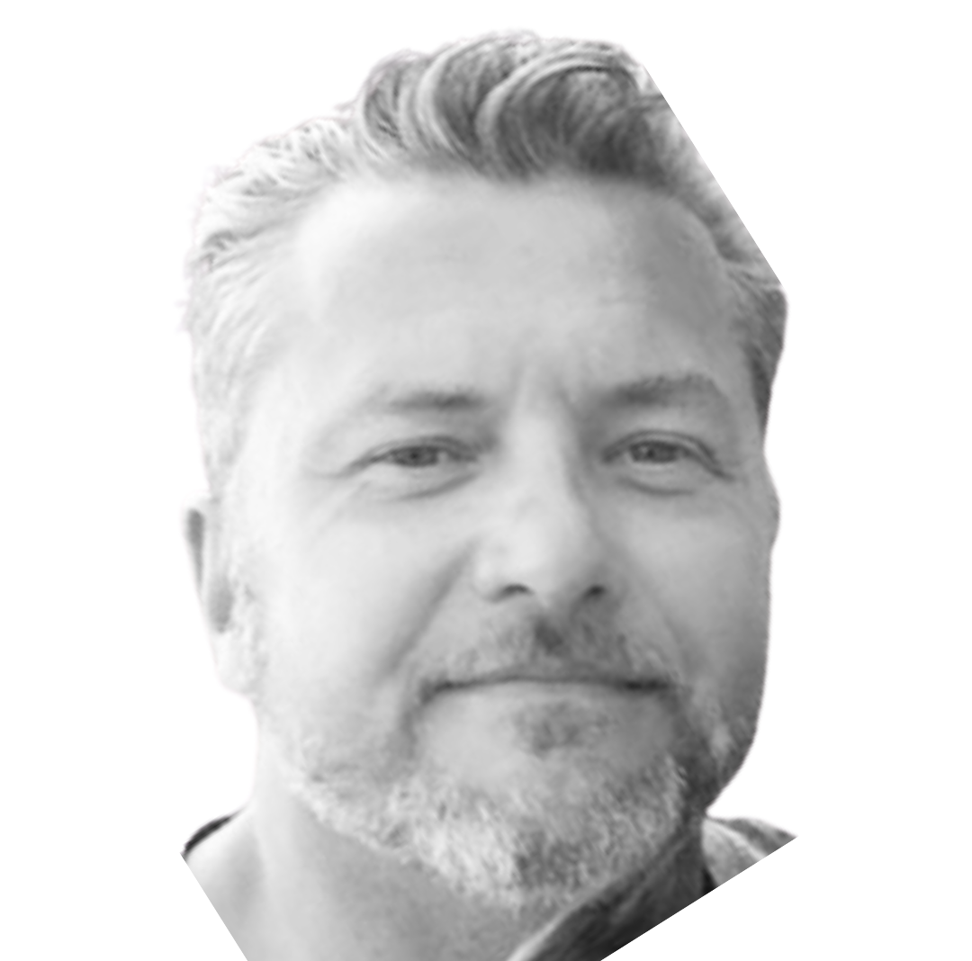 Photo of a smiling bald man wearing a suit, outdoors with a blue sky in the background.