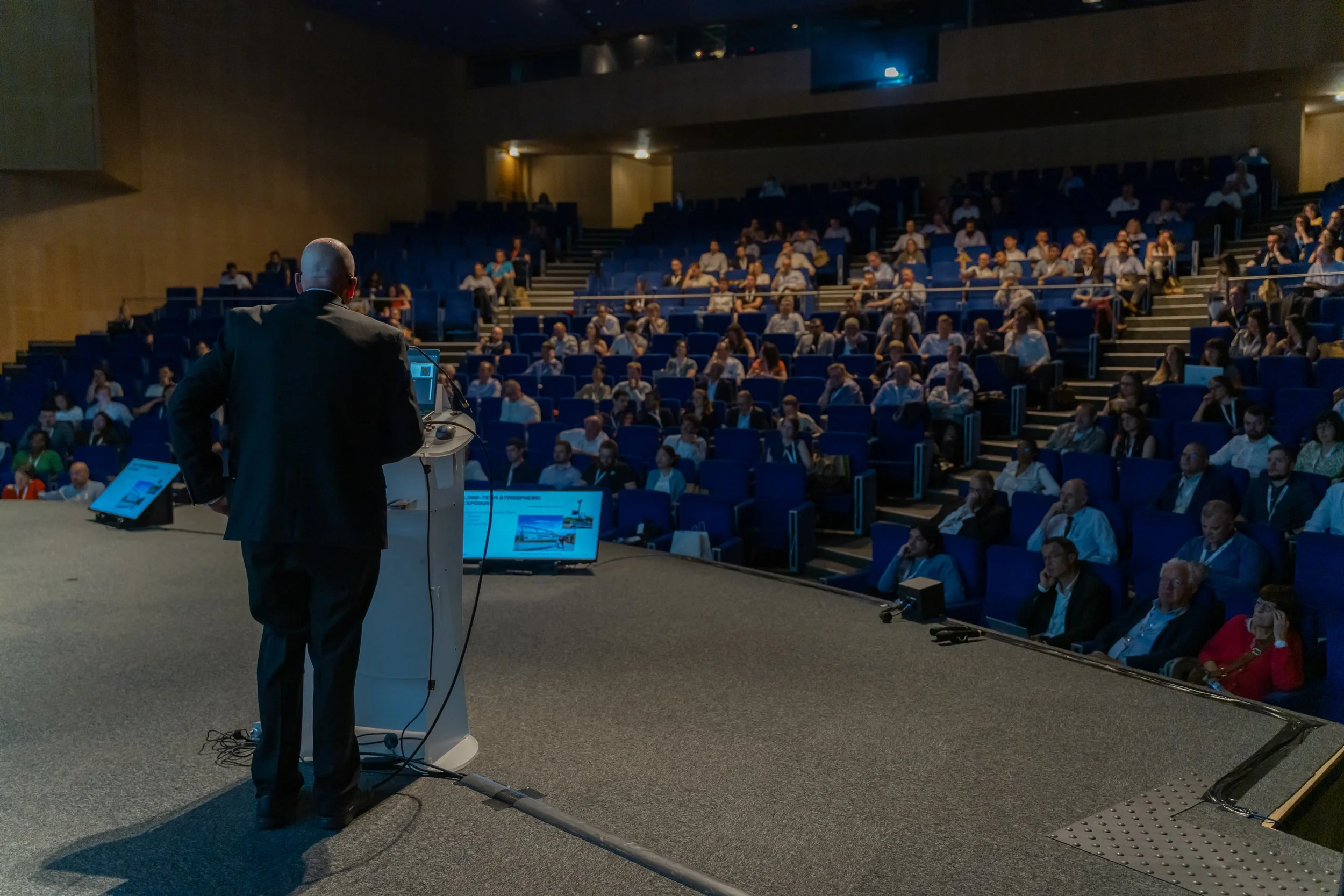 Un conférencier sur scène devant un public dans un auditorium.