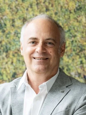 Portrait of a smiling person in front of a wooden shelf.