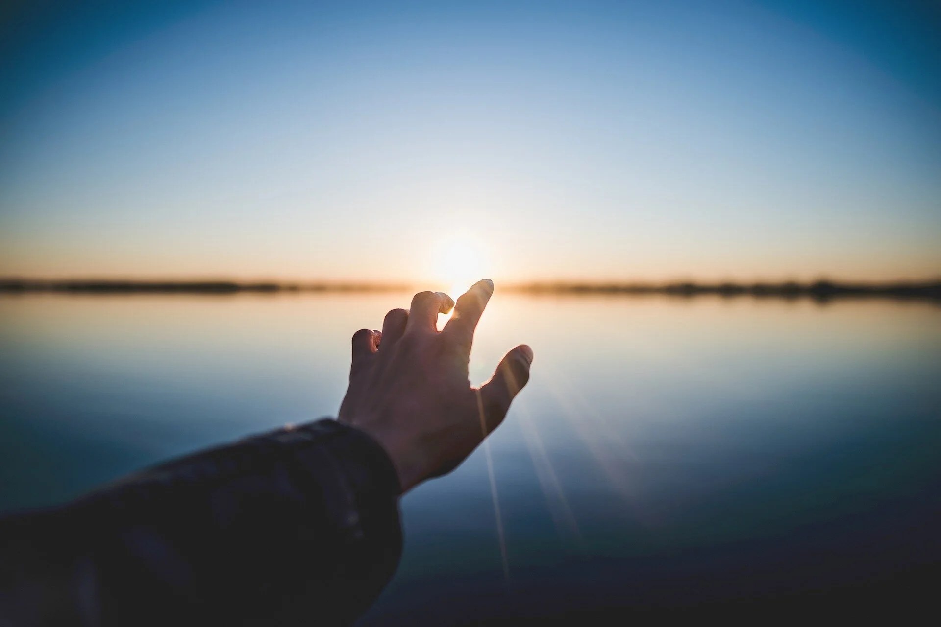 Hand pointing at sunset and horizon above lake